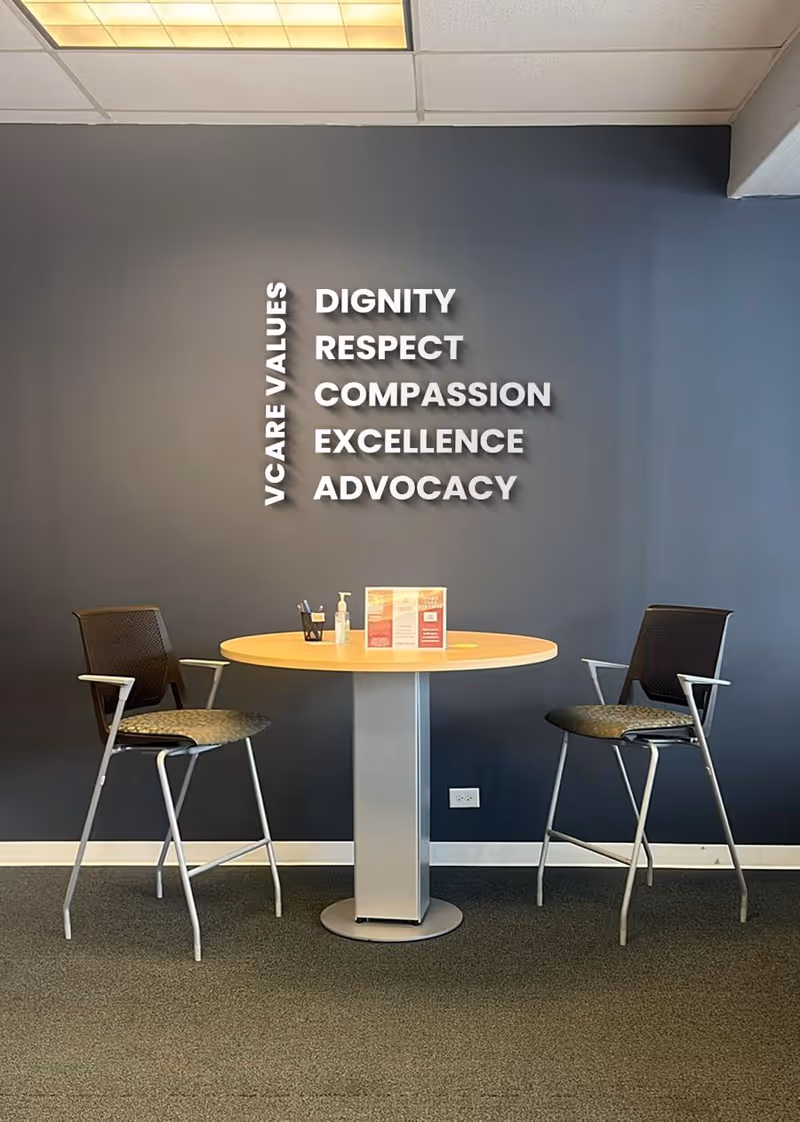 Two chairs flank a round table against a blue wall with VCARE VALUES.