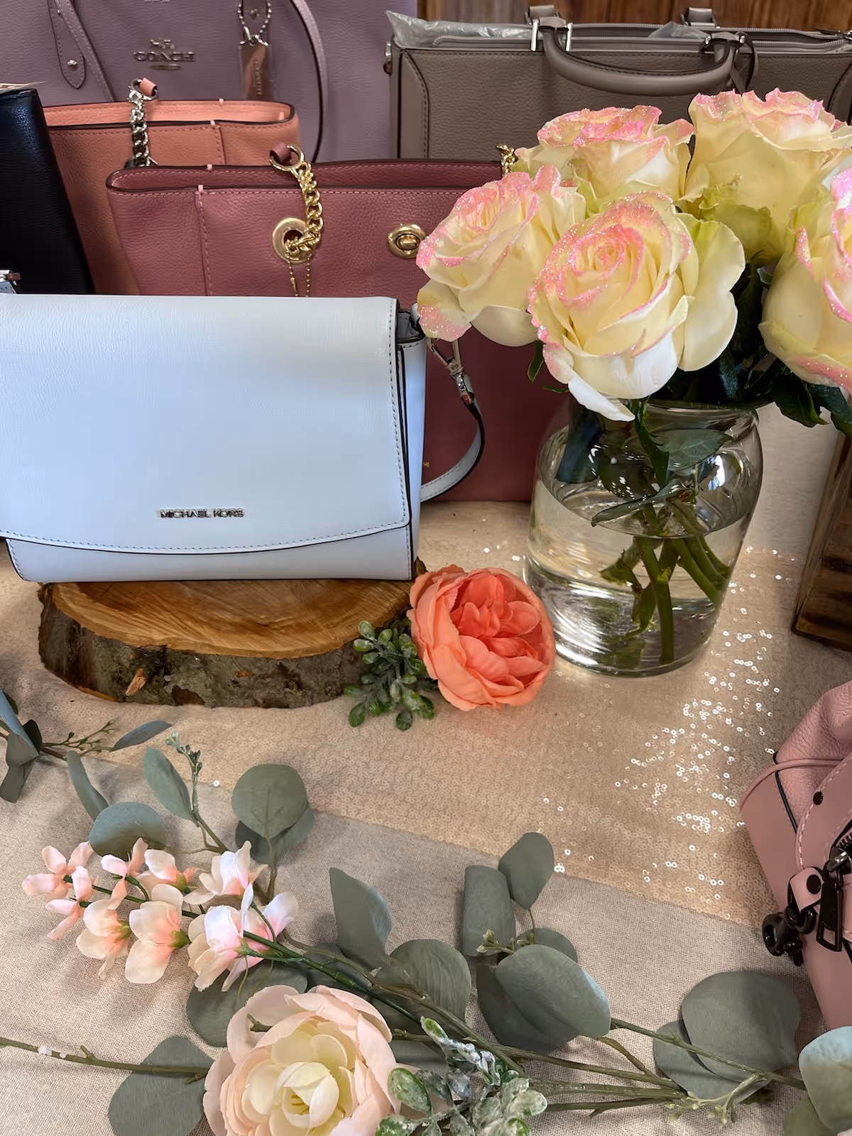 Assorted pastel handbags and roses arranged on a wood slice display indoors.