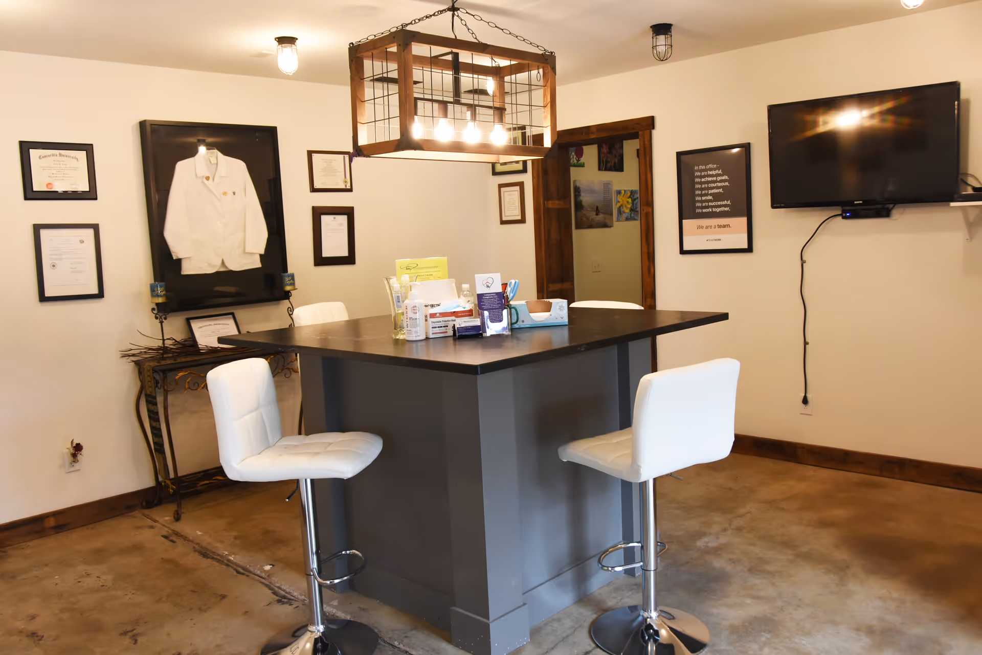 Lounge-style reception area with a tall counter, white stools, framed certificates, and a mounted TV.