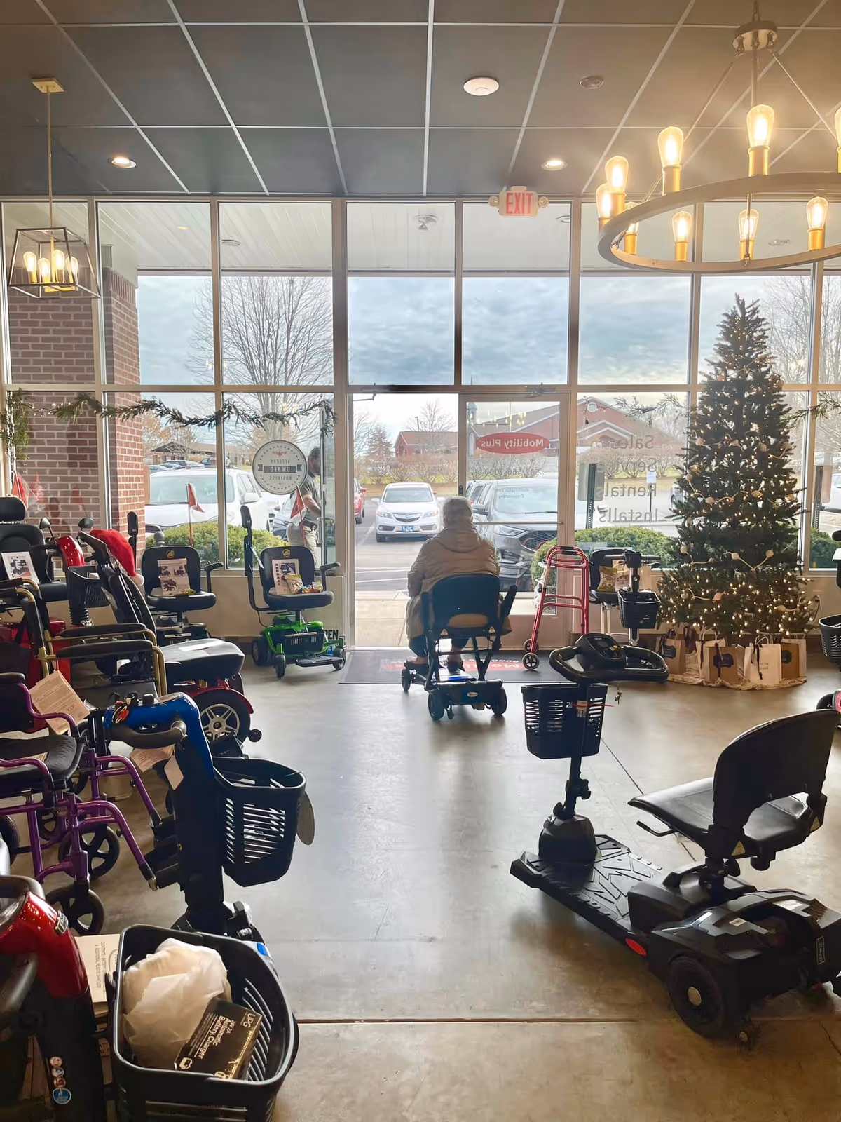 Interior showroom with mobility scooters, walkers, and a decorated Christmas tree by large windows.