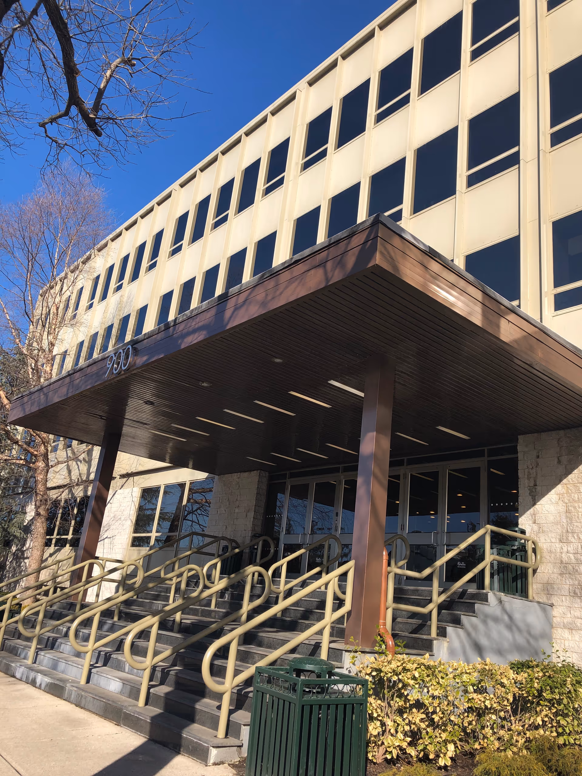 Exterior view of a building entrance with a covered canopy and rail stairs.