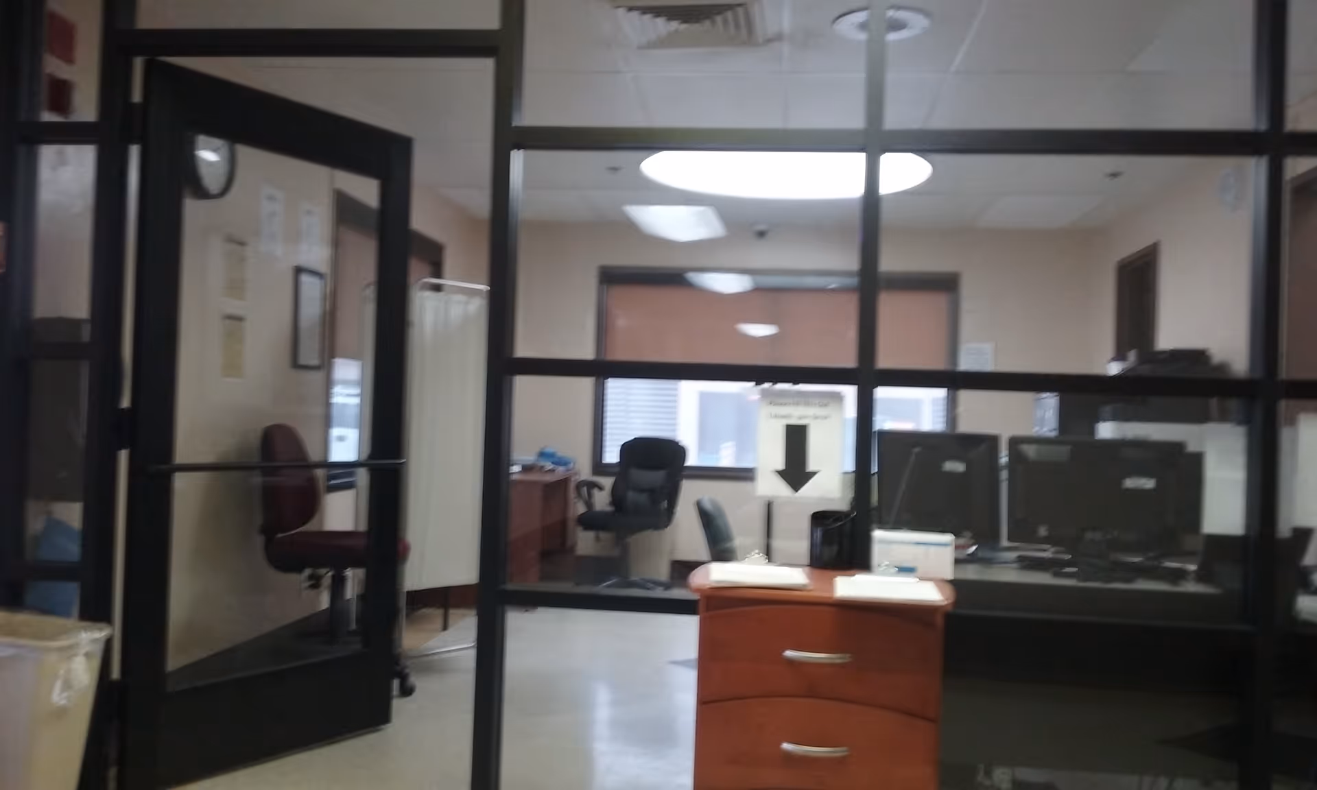 Office reception area inside a facility, with glass partition, desk, and computer monitors.