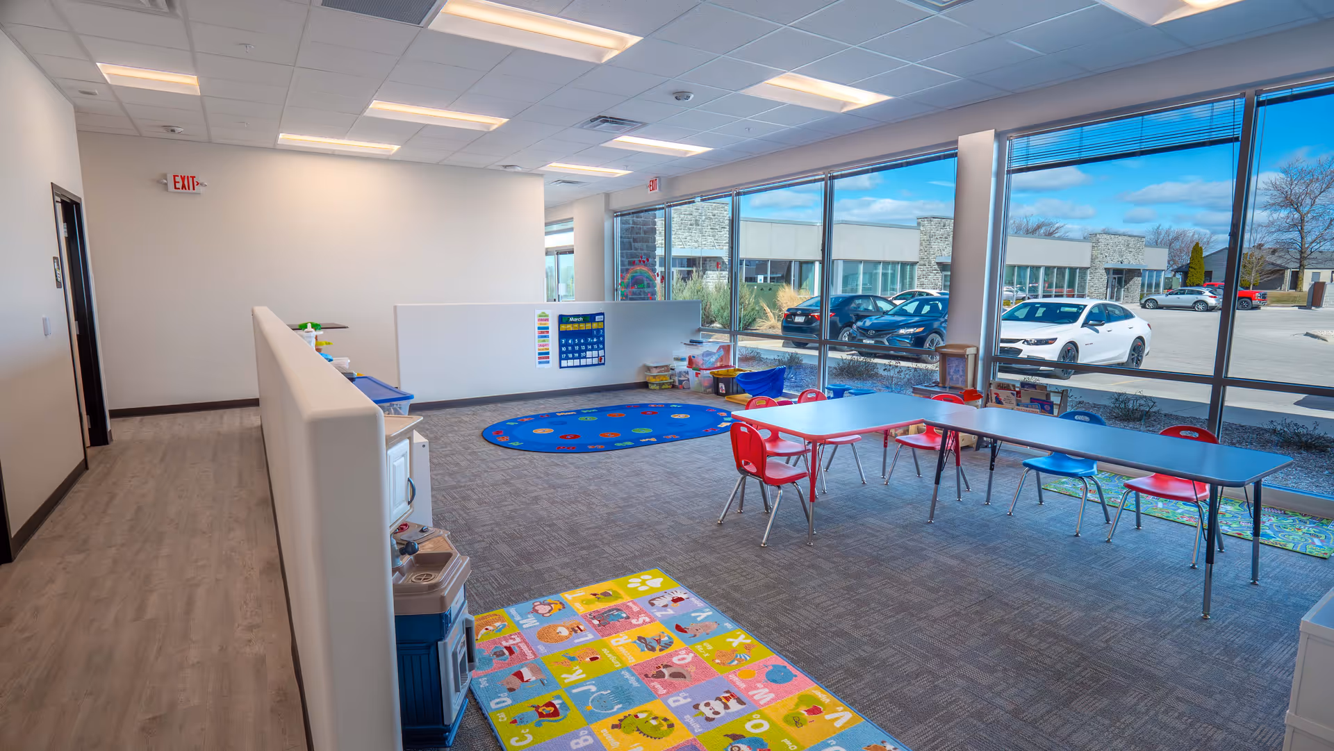 Bright open room with large windows, child-sized tables and colorful play mats.