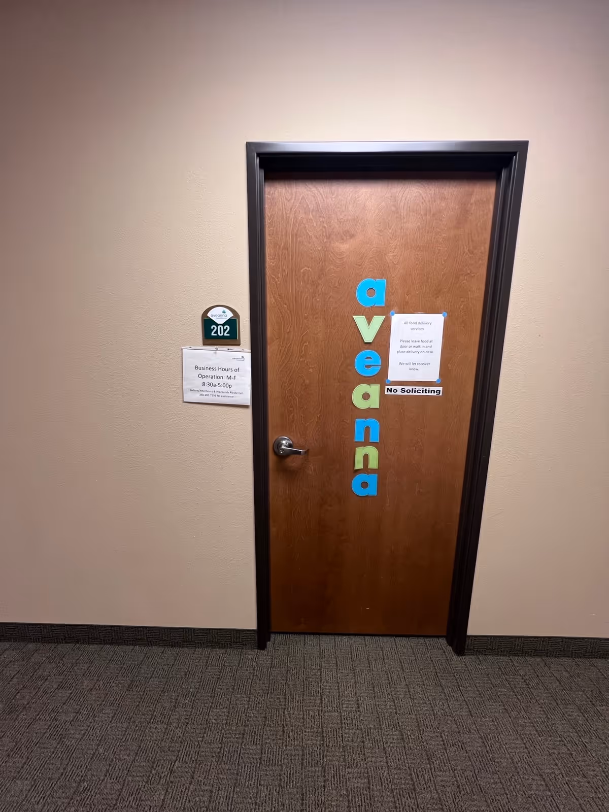 Wooden interior door with Aveanna letters and room number plaque in a hallway.