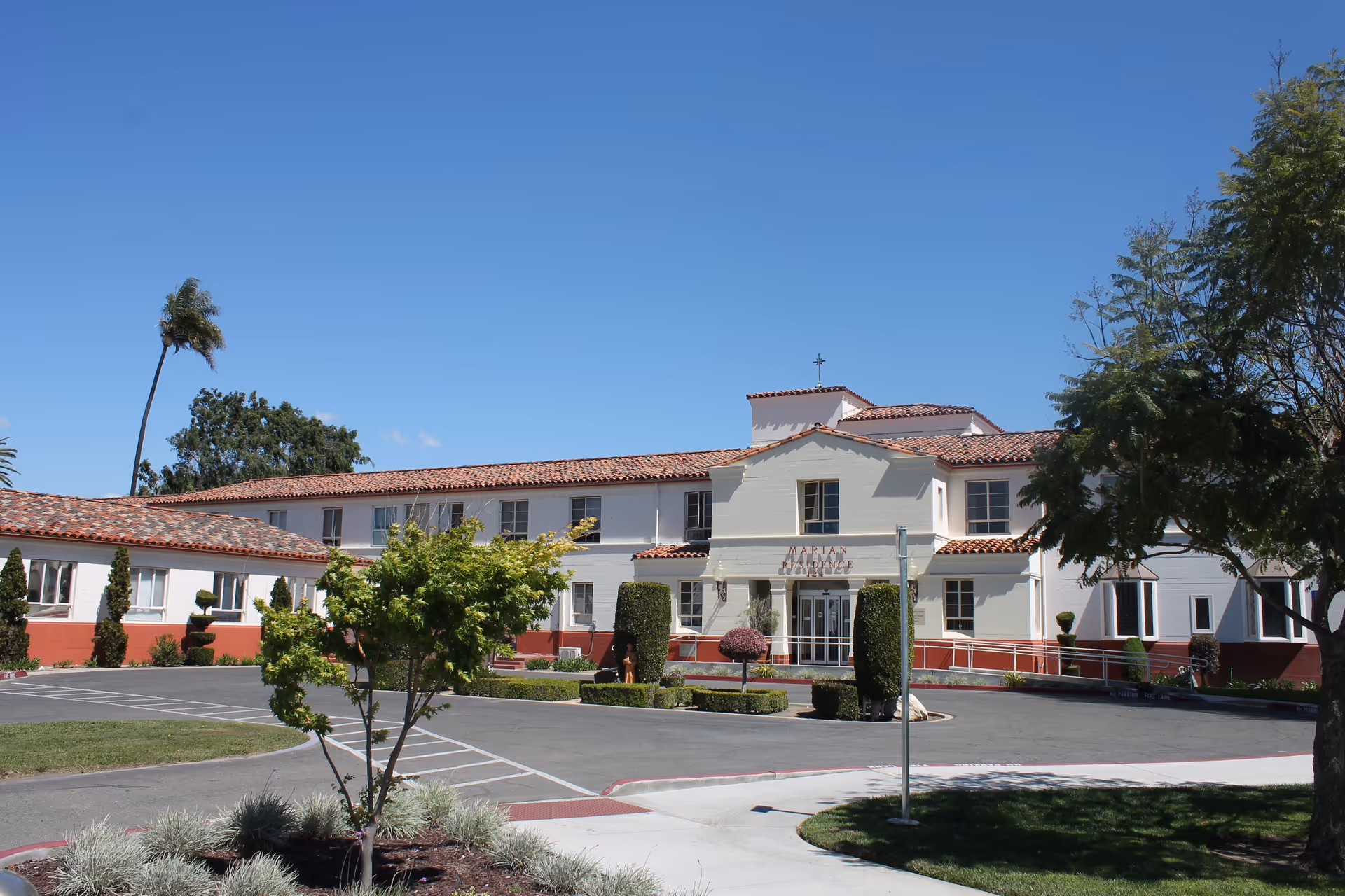 Exterior view of a white building with a red-tiled roof and manicured landscaping.