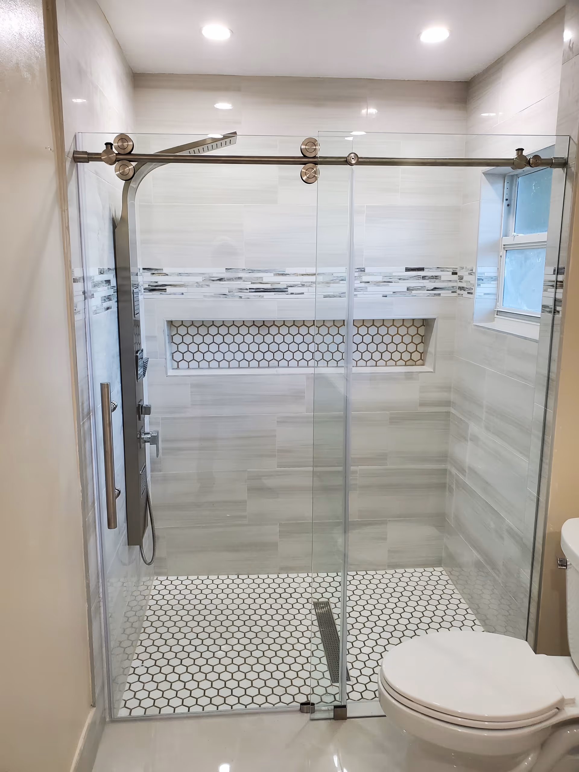 Modern glass-enclosed bathroom with shower, built-in niches, and a toilet.