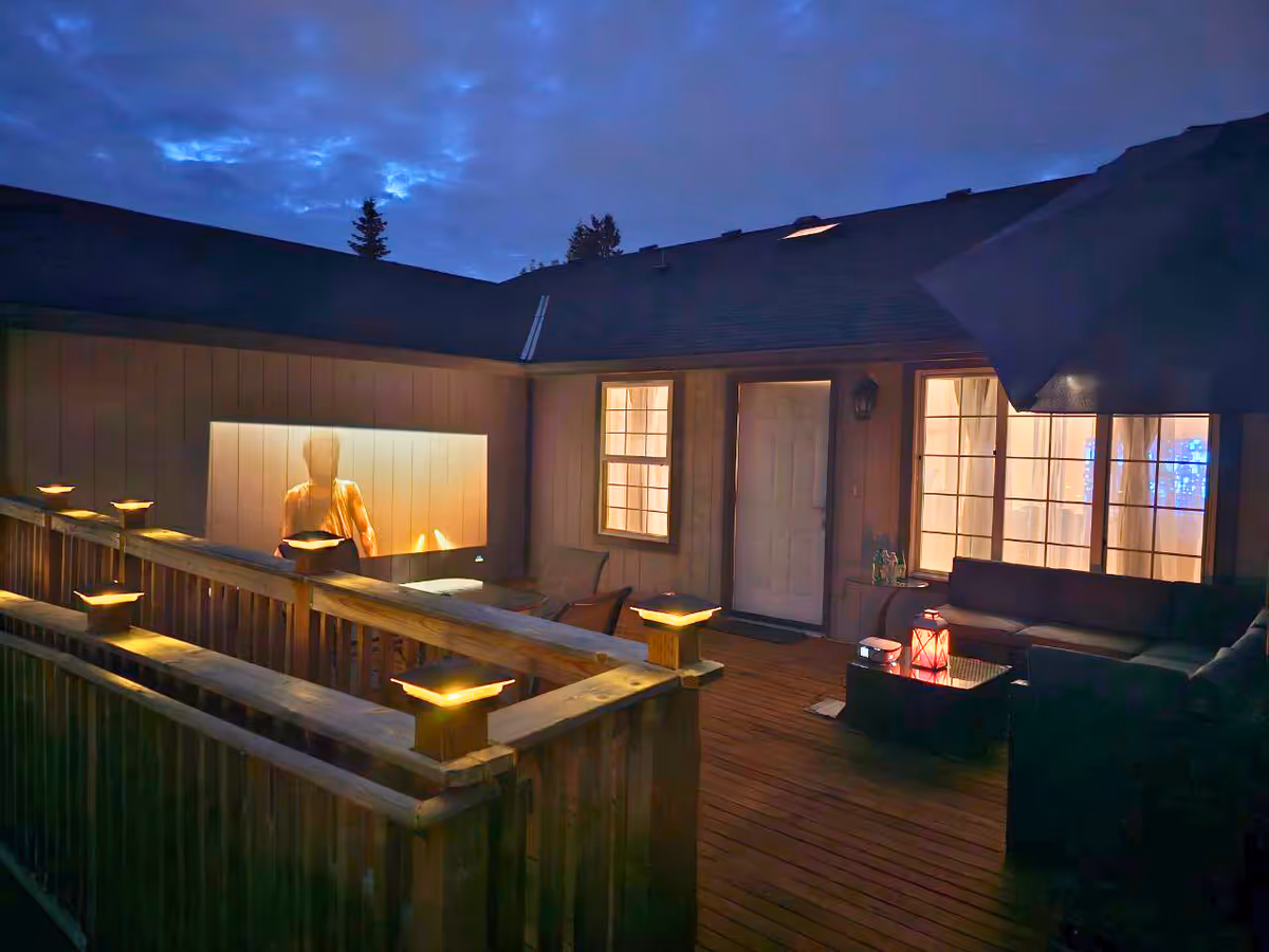 Wooden outdoor deck with seating and lanterns outside a senior living facility at dusk.