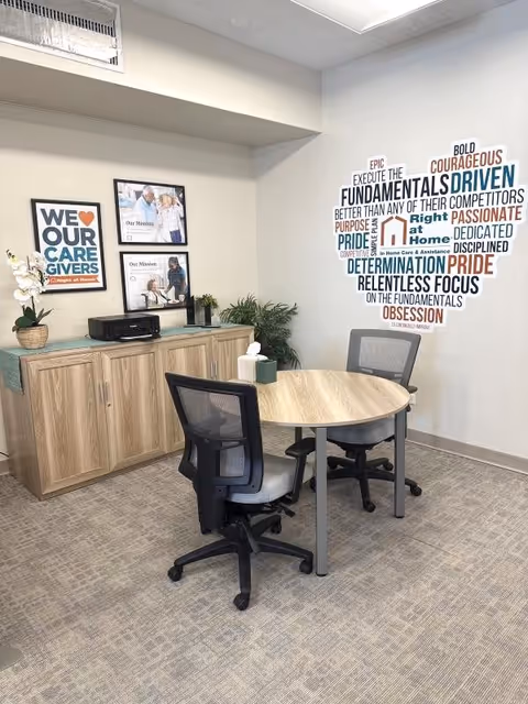 A small interior meeting room with a round table, chairs, a wooden cabinet, and wall art.