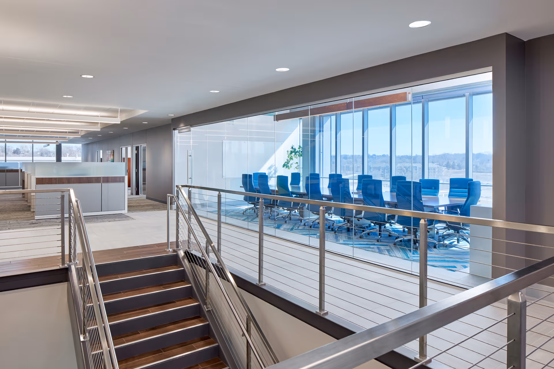 Modern interior with stairway and glass-walled conference room featuring blue chairs.