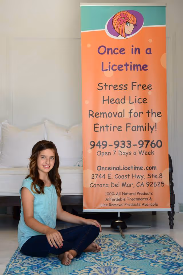 Young girl sits on a blue rug beside an orange banner advertising lice removal services.