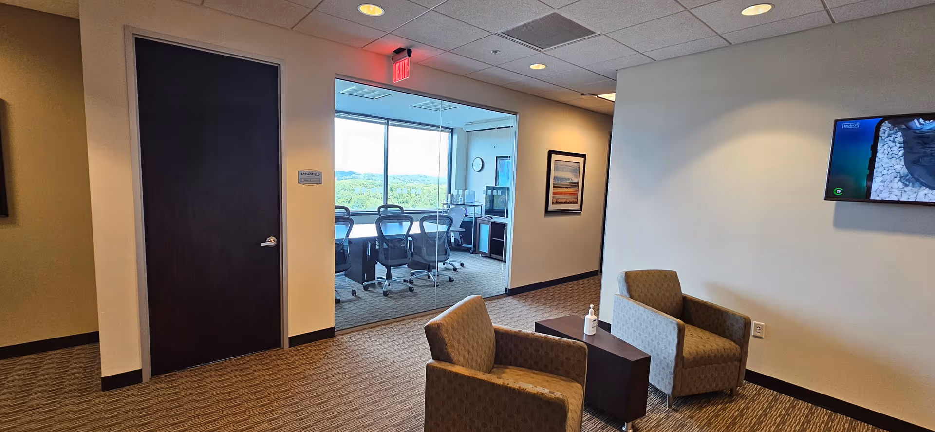 Senior living facility lounge with two armchairs, a side table, and a conference room visible.