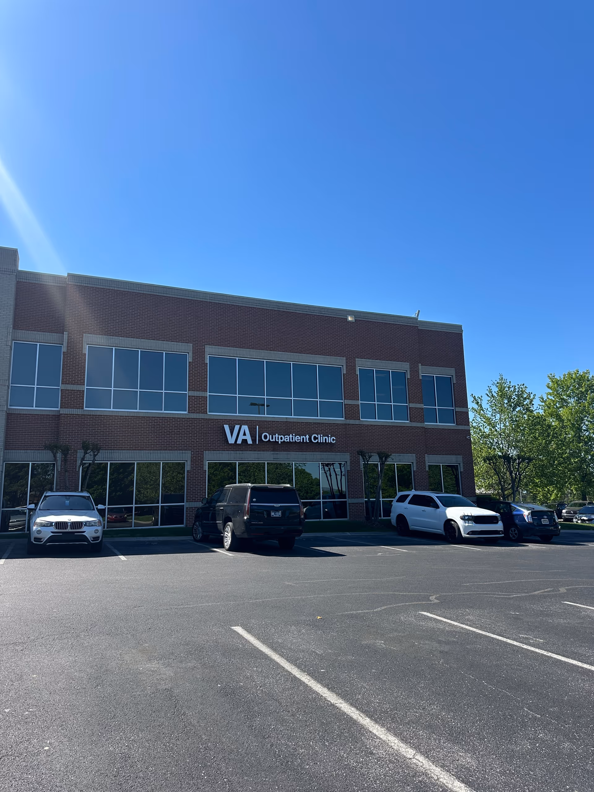 Brick two-story VA Outpatient Clinic building with large windows beside a parking lot.