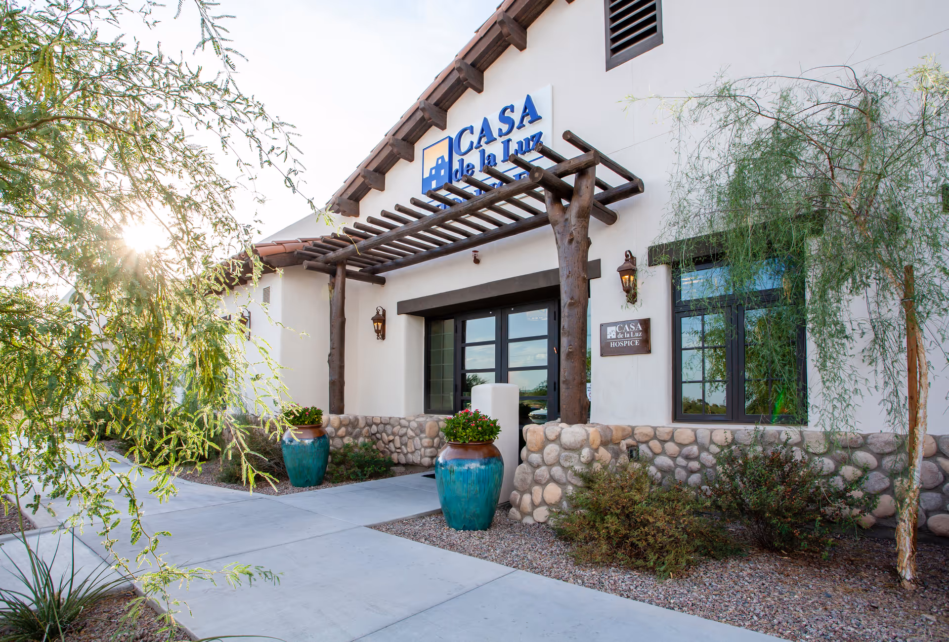 Exterior view of Casa de la Luz Hospice entrance with stone base, pergola, and potted plants