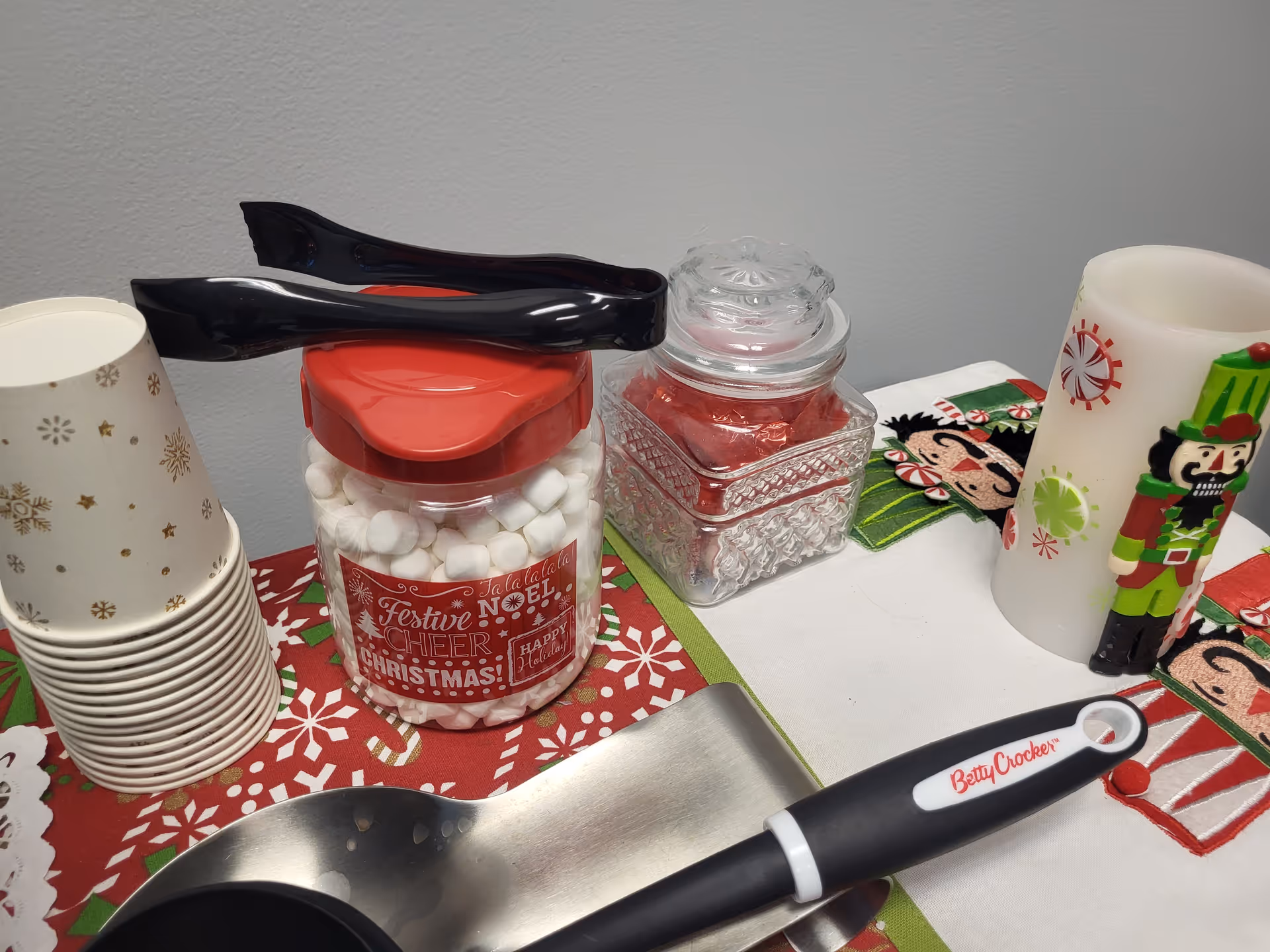 Holiday themed table with marshmallows, a glass jar, festive cups, and a spatula.