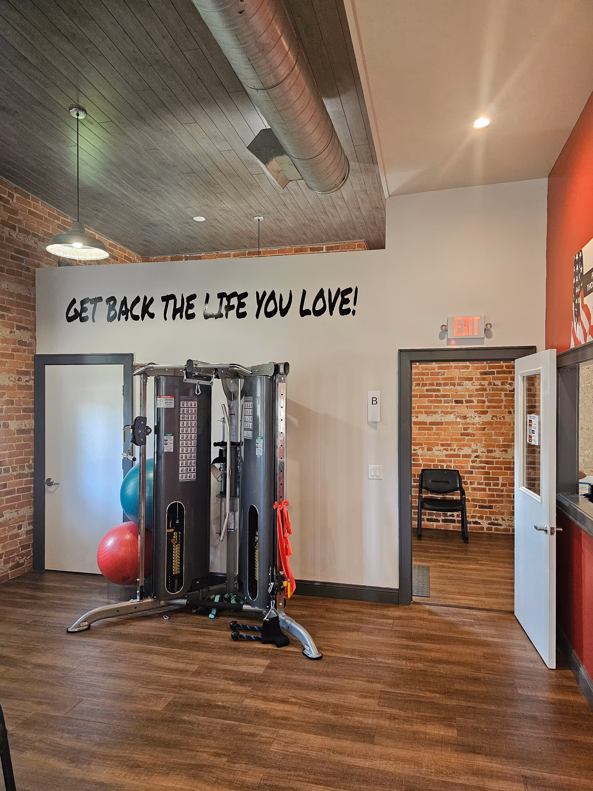 Industrial-style gym room with exercise machines, brick walls, and a motivational slogan.