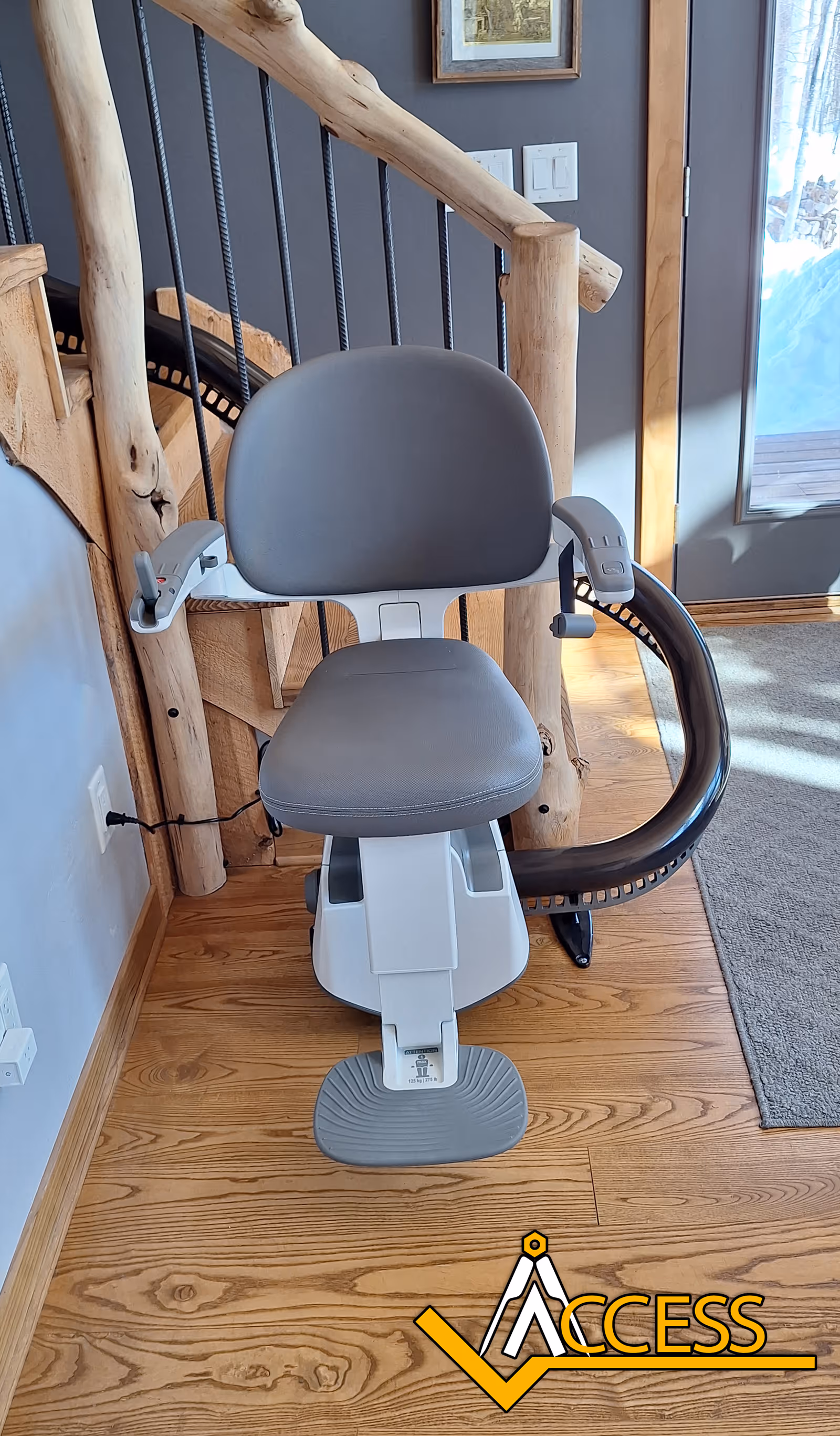 Grey stairlift chair mounted beside a wooden staircase inside a residential facility.
