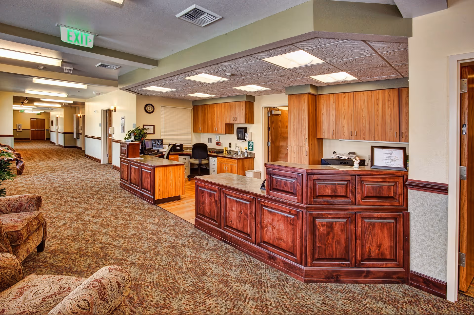 Interior of a senior living lobby with a wood reception desk, cabinets, and hallway.