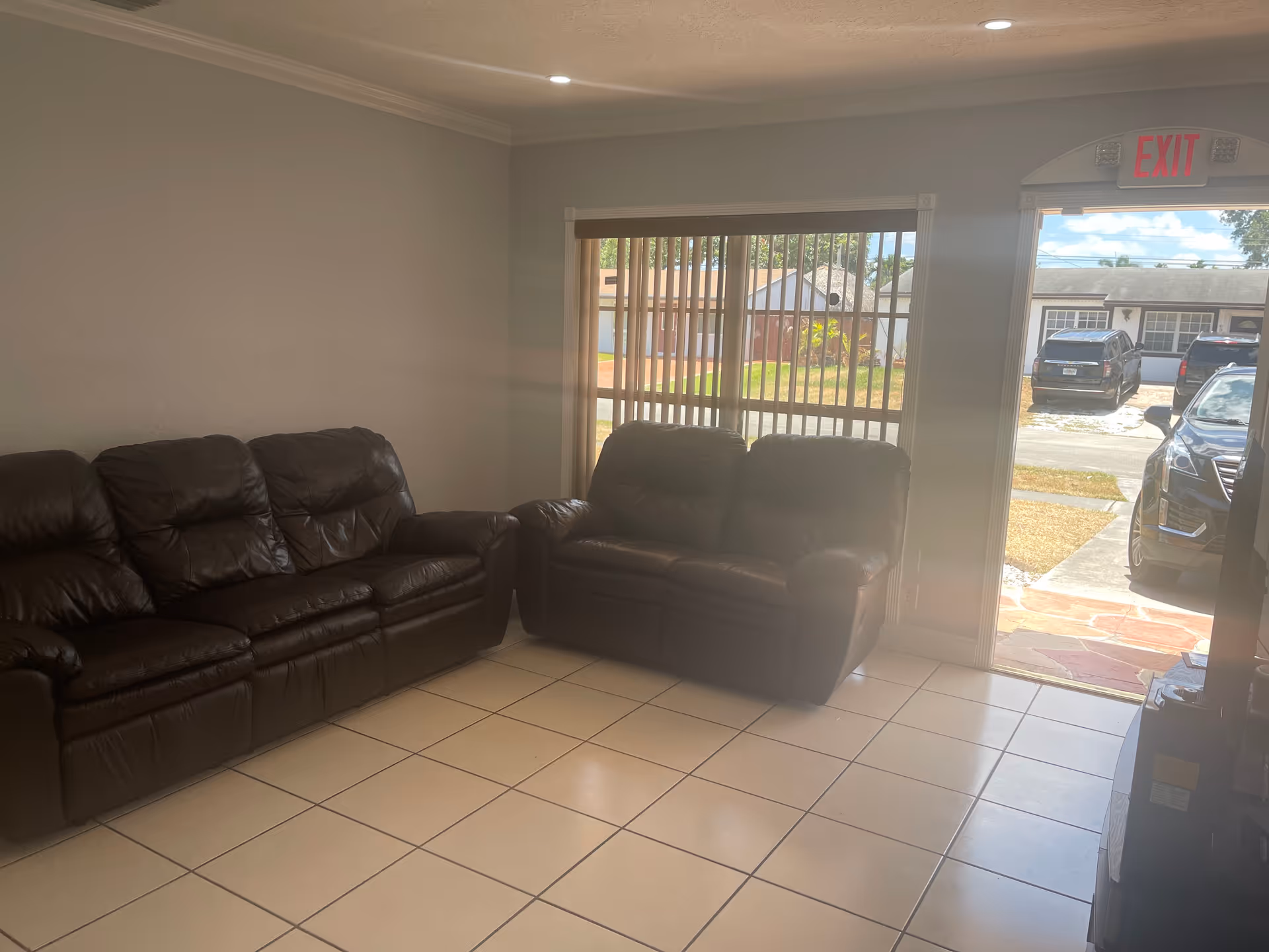 Bright living room with black leather sofas, tiled floor, and a glass door to outdoors.