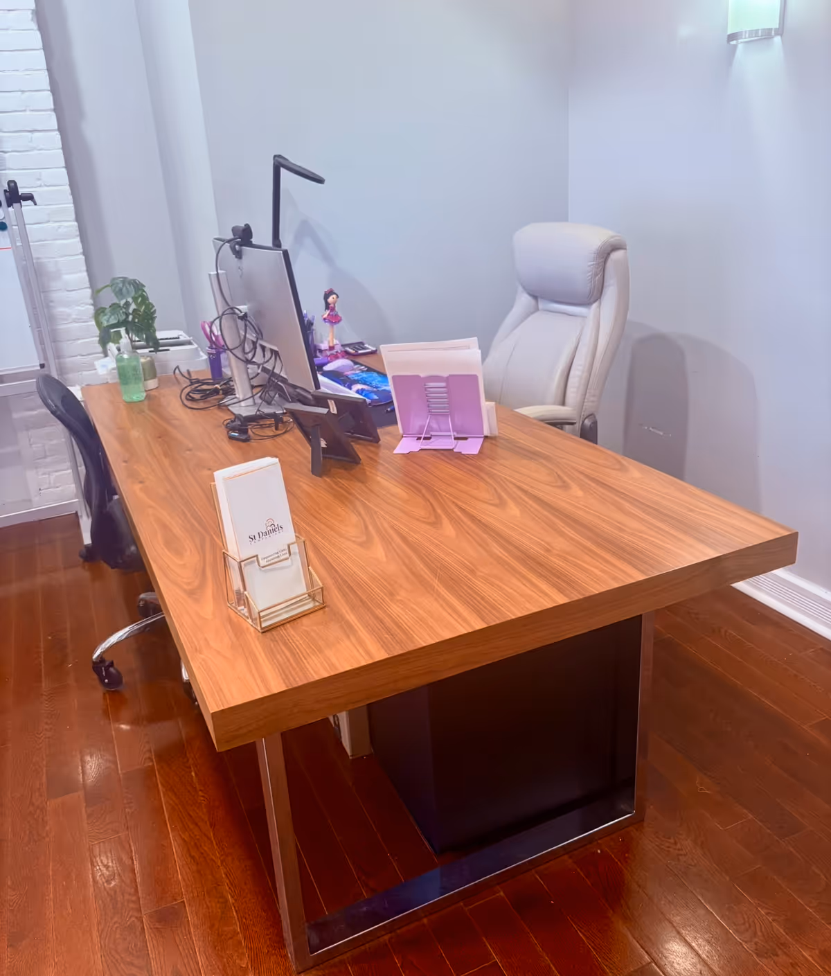 A wooden desk with computer, cables, plant, and pink folders in an office.