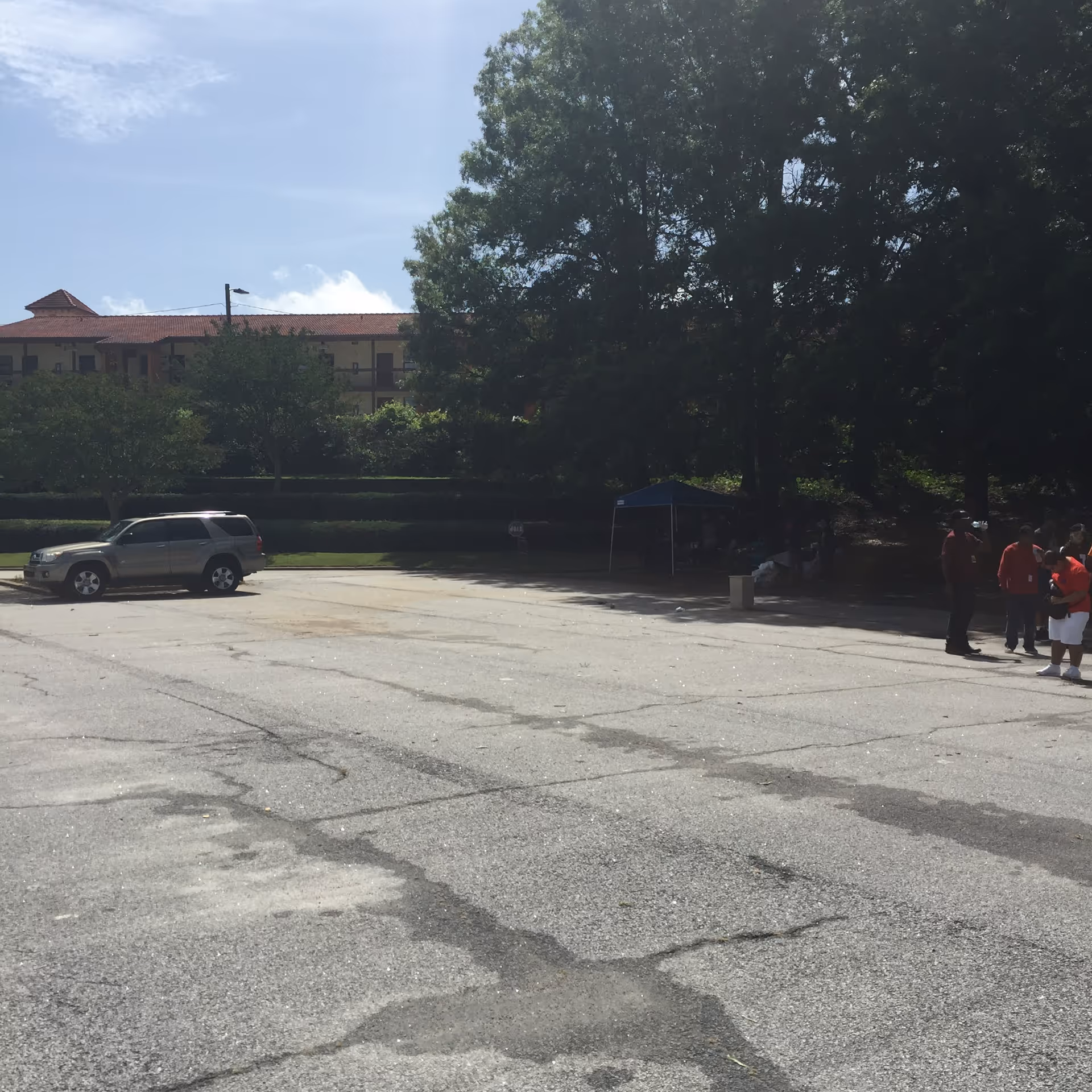 Outdoor parking lot in front of a building with trees and a small group of people.