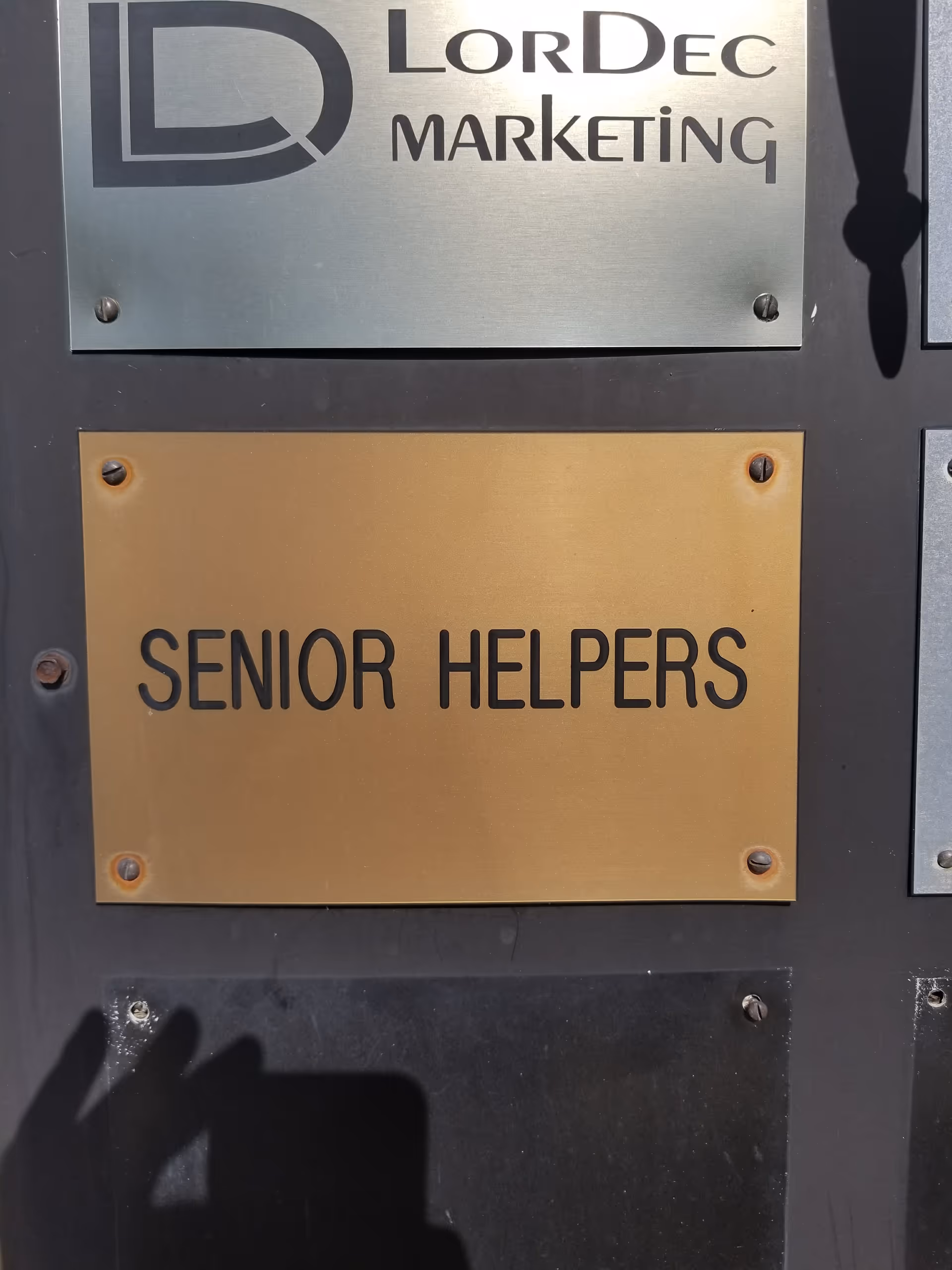 Exterior wall with brass plaque reading 'Senior Helpers' beside a marketing sign.
