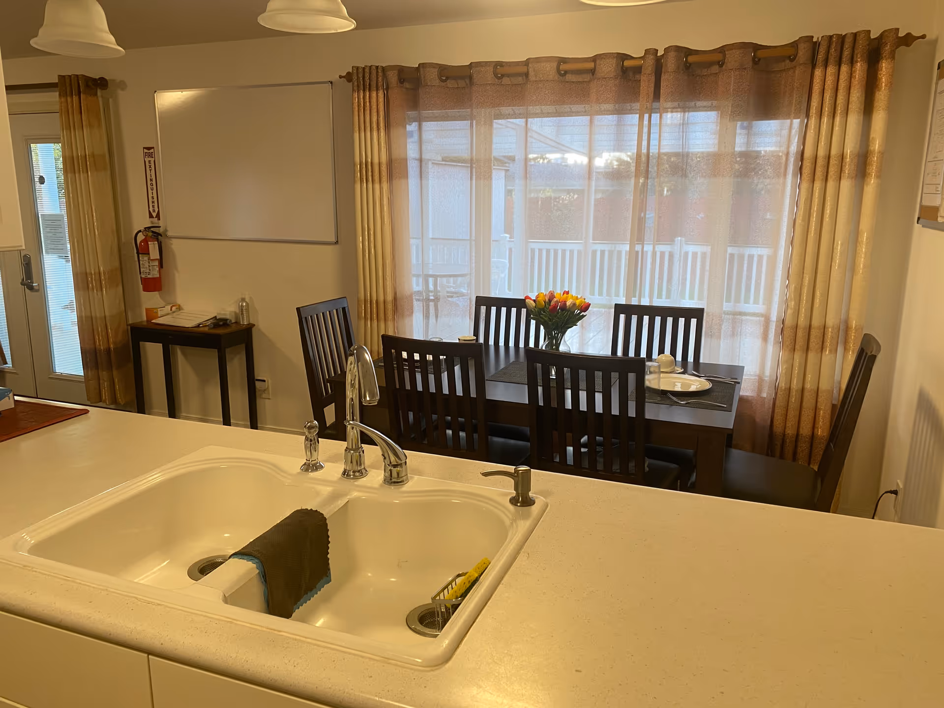 Open-plan kitchen and dining area with sink, table, chairs, and large curtained windows.