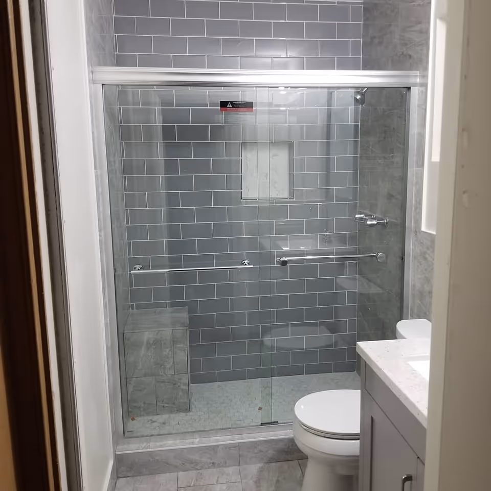 Gray tiled bathroom with a glass shower enclosure, toilet, and white vanity.