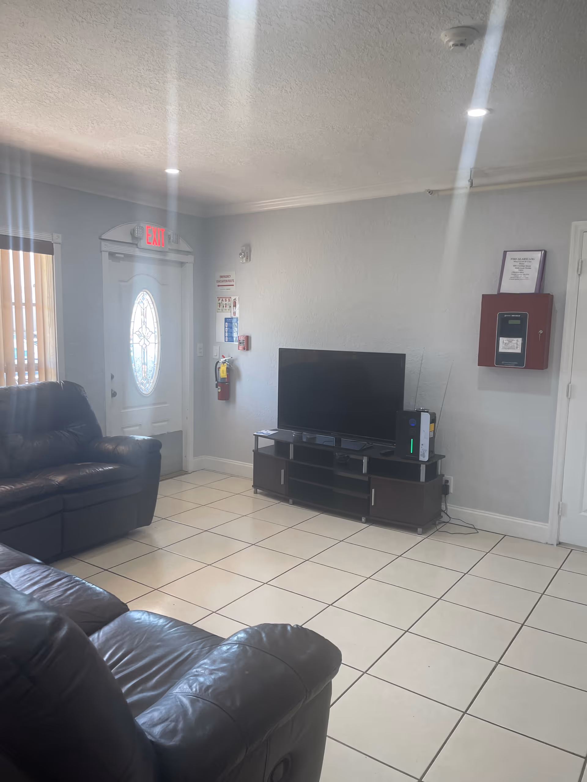 Living room in a facility with leather couches, TV on a stand, and exit door.