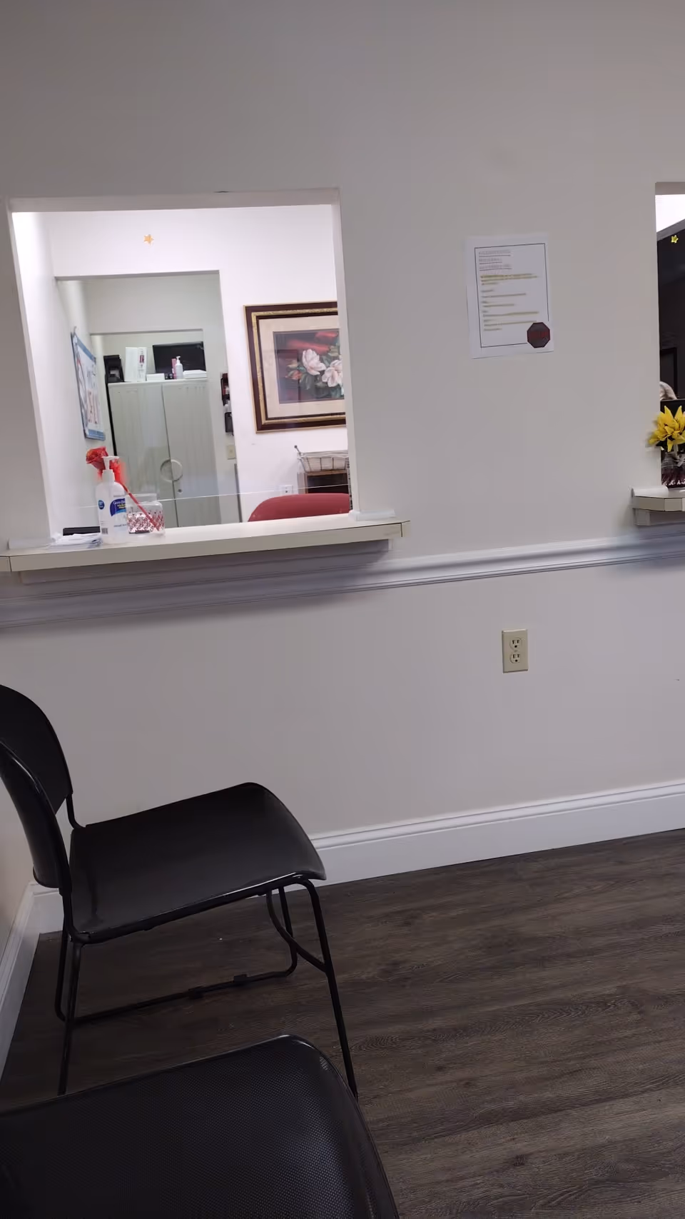 Interior facility reception area with window counter, a black chair, wall art, and cleaning supplies.
