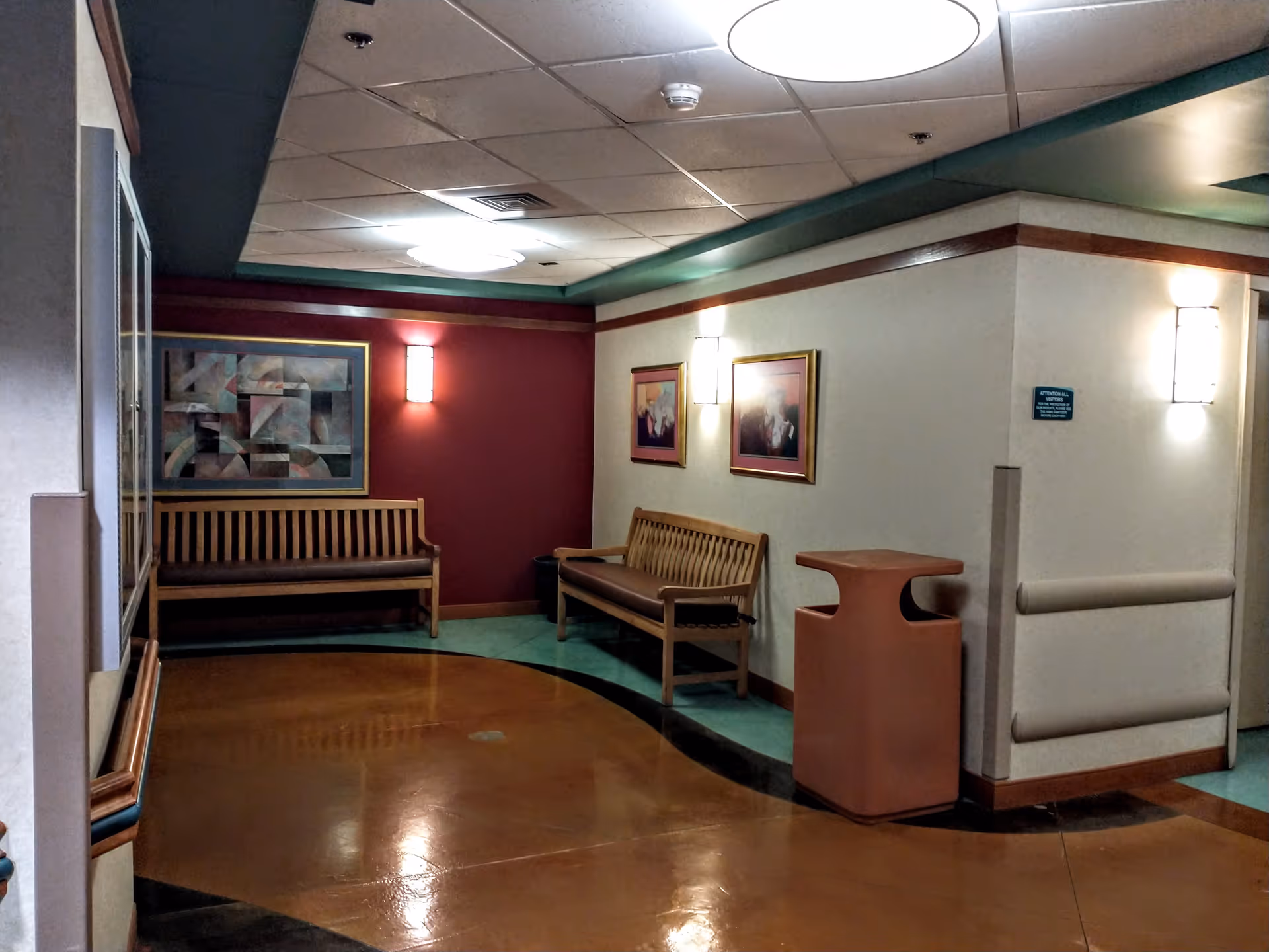 A hospital-like interior waiting area with wooden benches, framed artwork, and soft lighting.