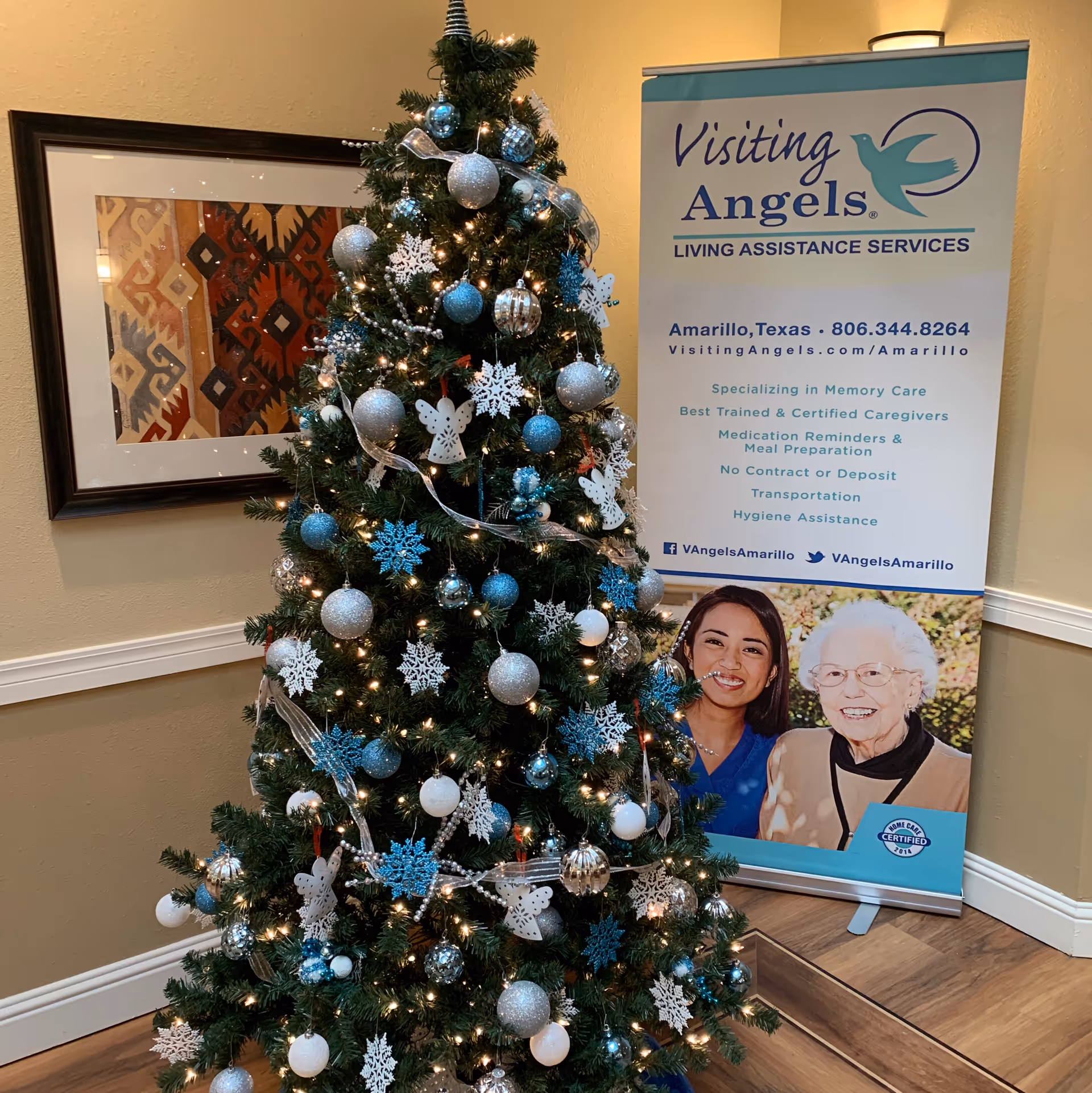 Indoor lobby with a decorated Christmas tree beside a Visiting Angels banner.