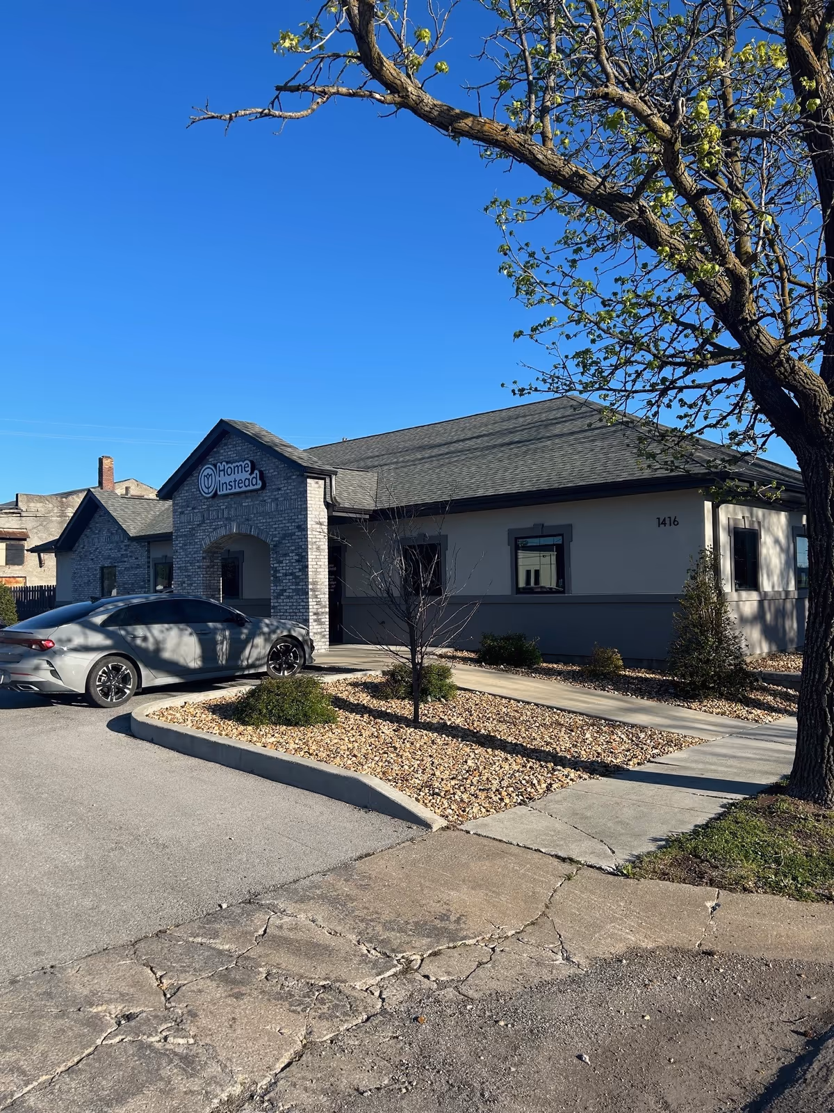 Exterior view of a Home Instead senior living facility with a driveway, sign, and trees.