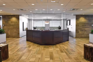 Polished lobby with wood floor, dark curved reception desk, and glass partition.