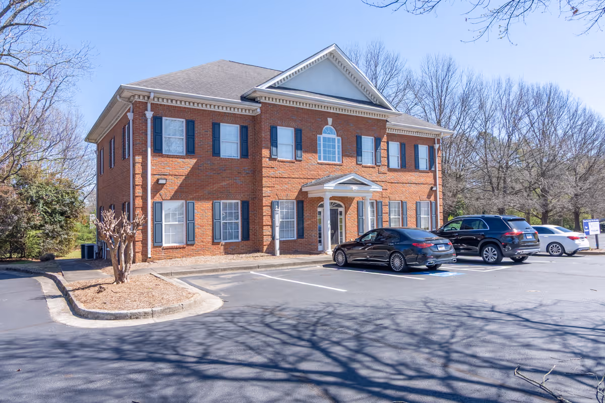 Red brick, two-story facility with blue shutters and several cars parked in front.