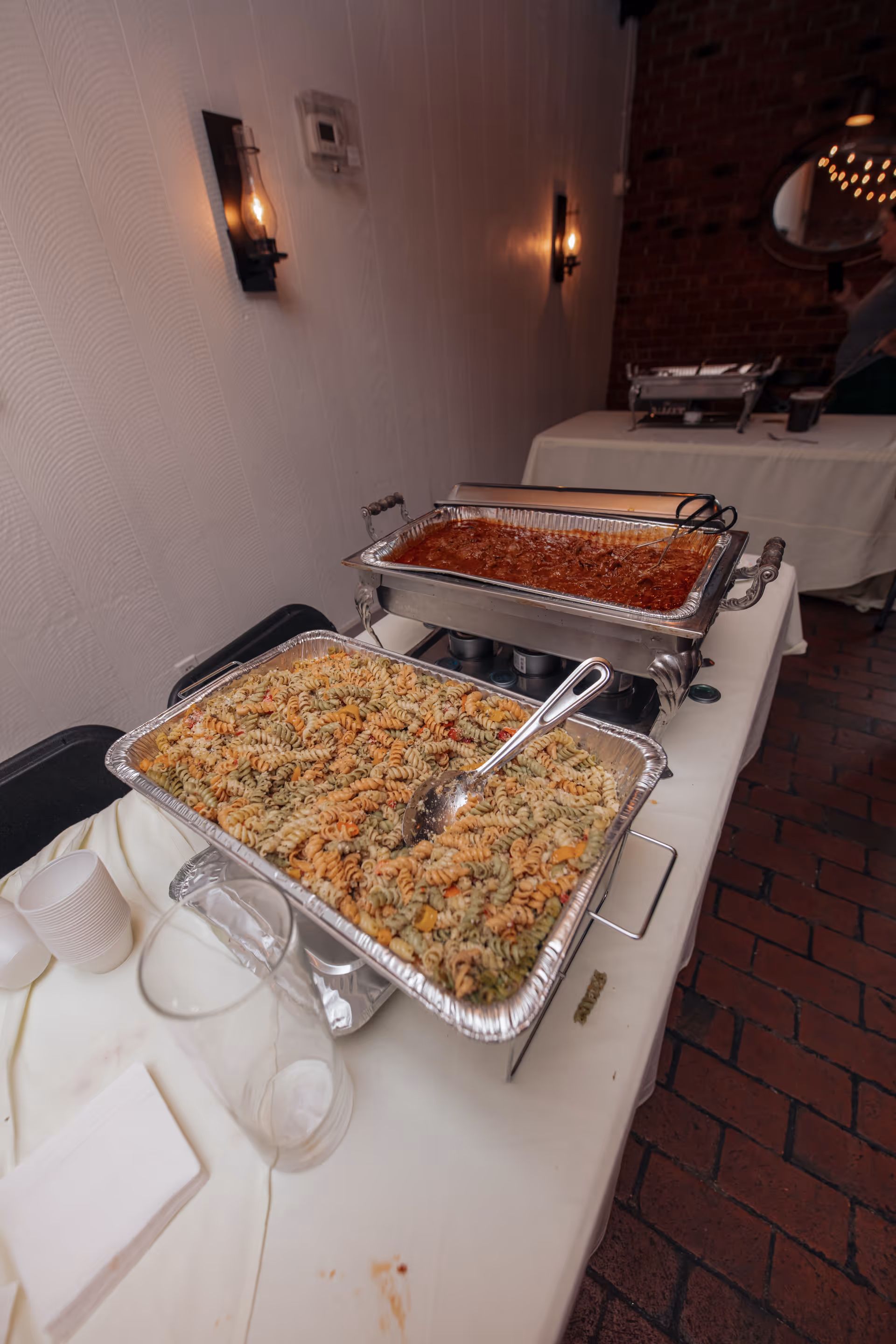 Buffet line with chafing dishes of pasta and sauce on a white table.