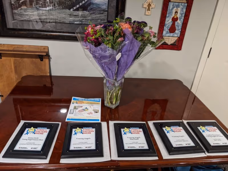 Awards plaques arranged on a polished wooden table with a purple bouquet in a room.