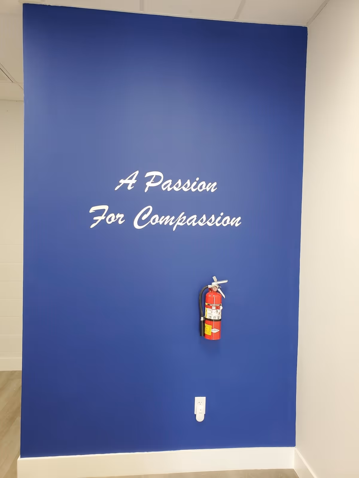 Blue interior wall with white script reading A Passion For Compassion and a fire extinguisher.