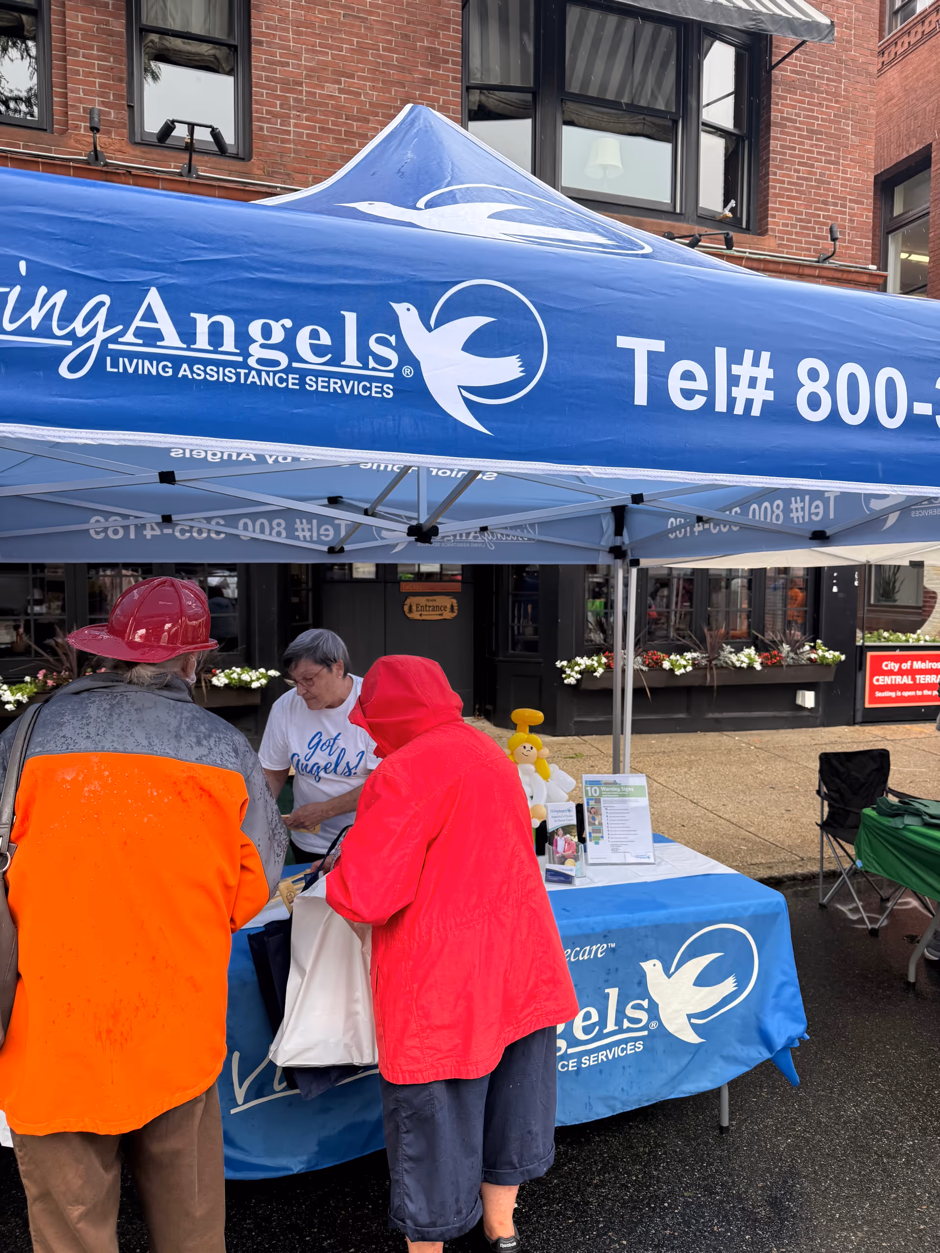 Outdoor information booth under a blue Visiting Angels tent with staff assisting visitors