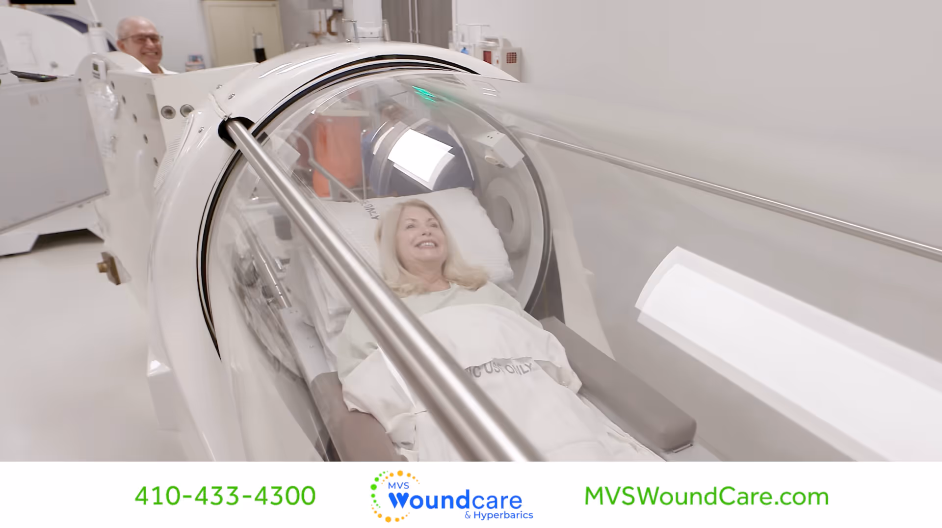 Patient lies in a hyperbaric chamber during wound care with a smiling staff member nearby.