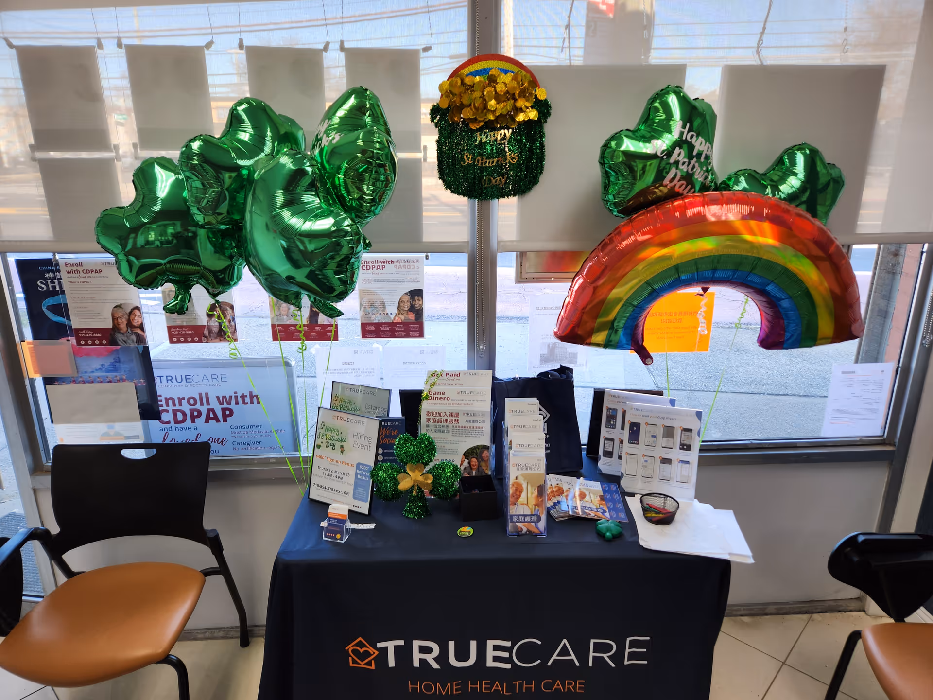 Promotional table with TrueCare signage, balloons, and brochures in a bright lobby.