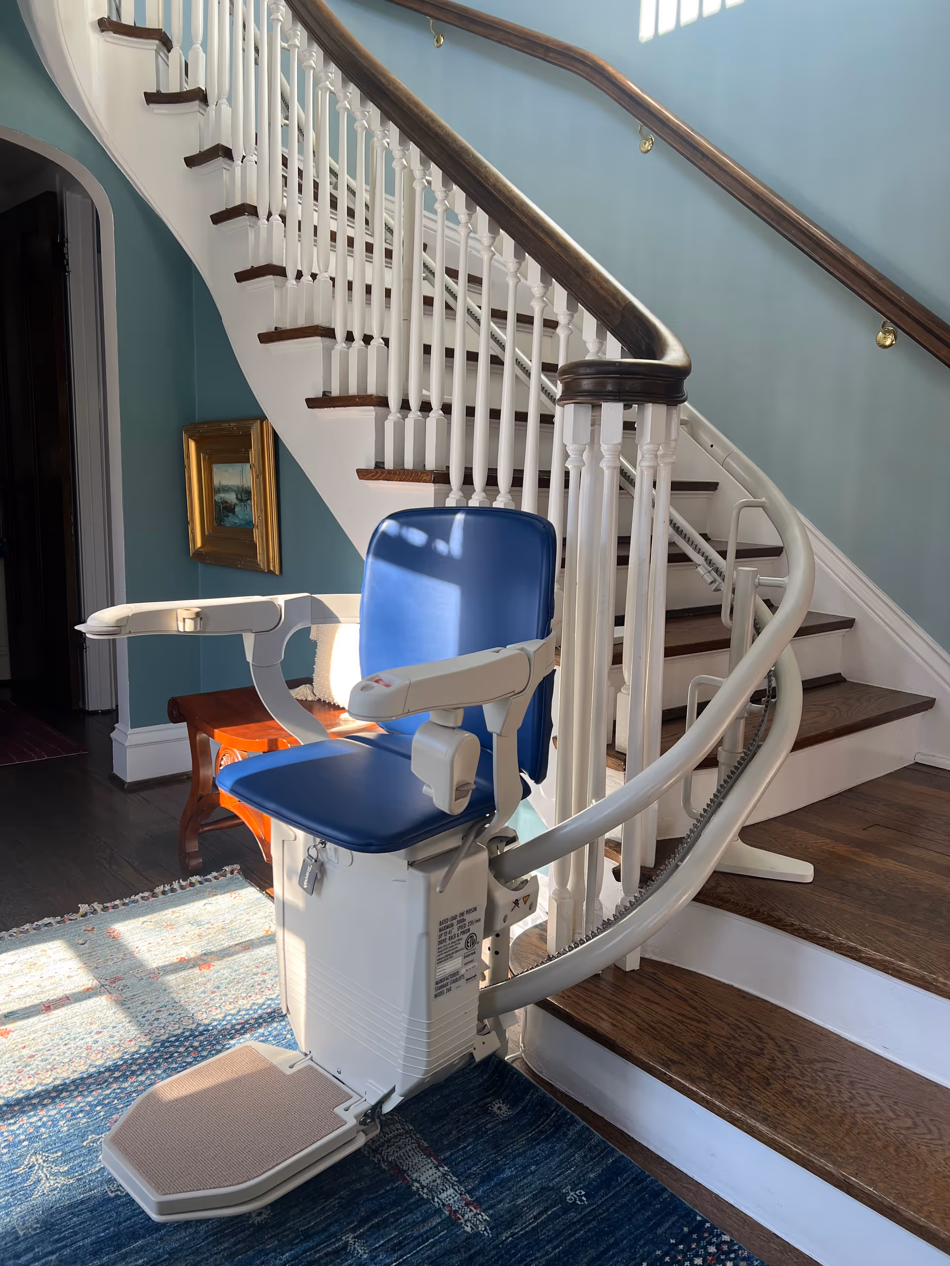 Interior staircase with a blue chair lift and curved railing beside teal walls.