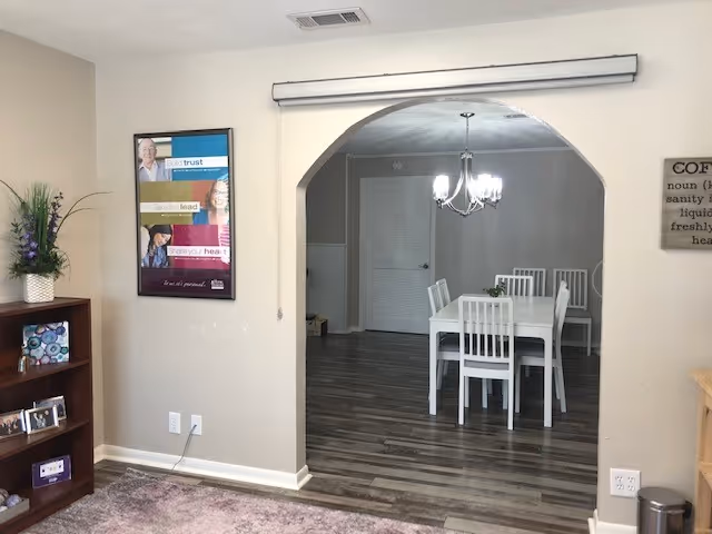 Interior dining room through arched entry with white table and chairs in a senior facility.