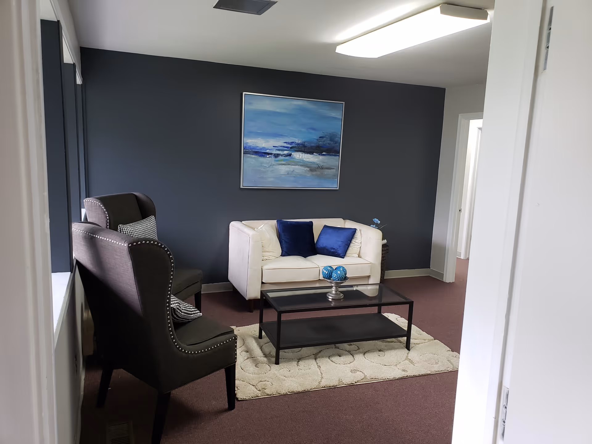 Cozy lounge with white sofa, dark chairs, blue wall, glass coffee table, and rug.