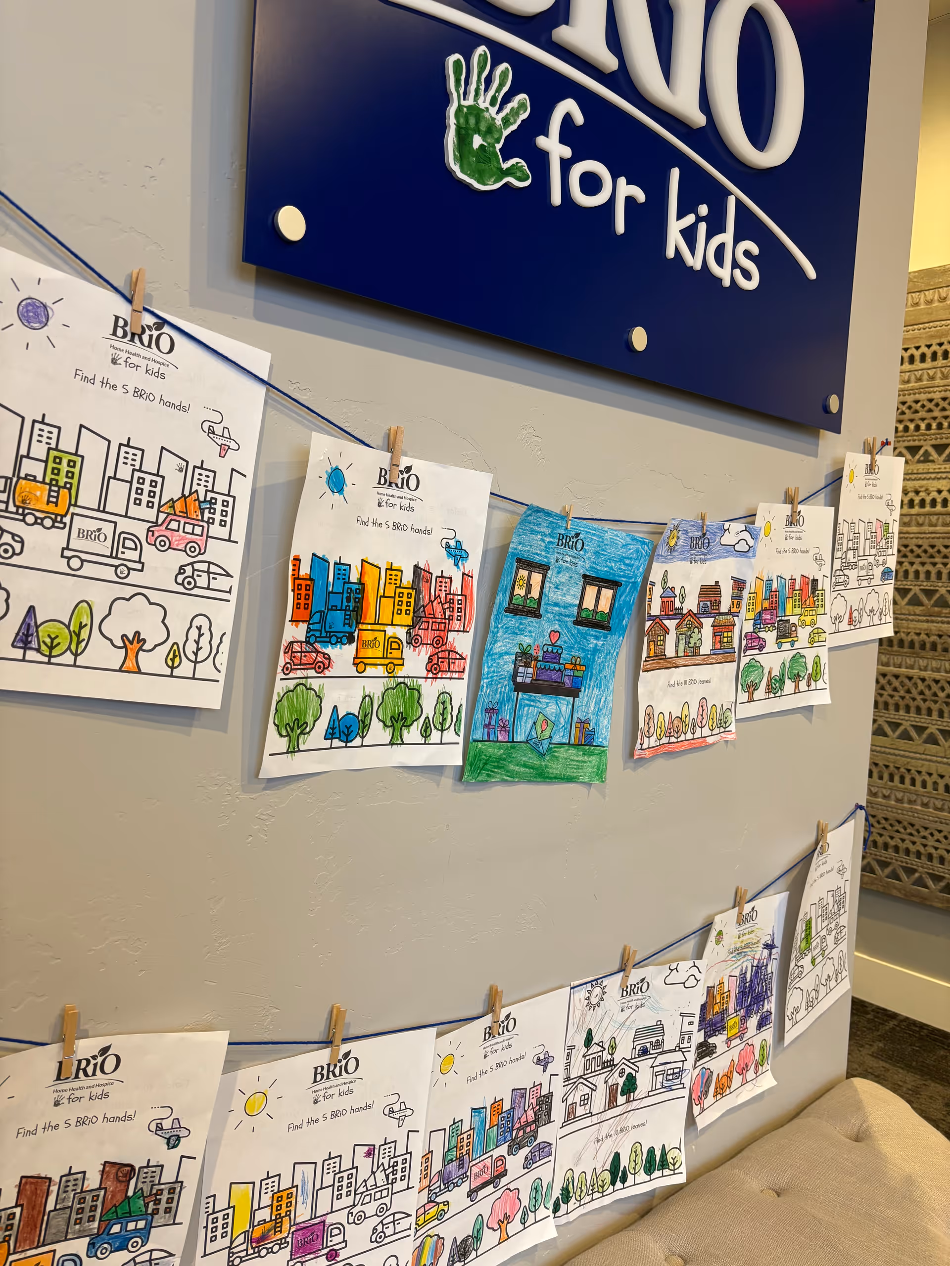 Colorful kids' drawings clipped to string along a wall beneath BRiO for kids sign.