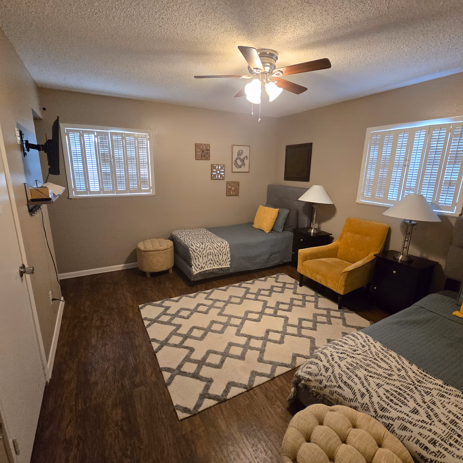 Cozy bedroom in a senior care home with two beds, nightstands, lamps, yellow chair, rug.