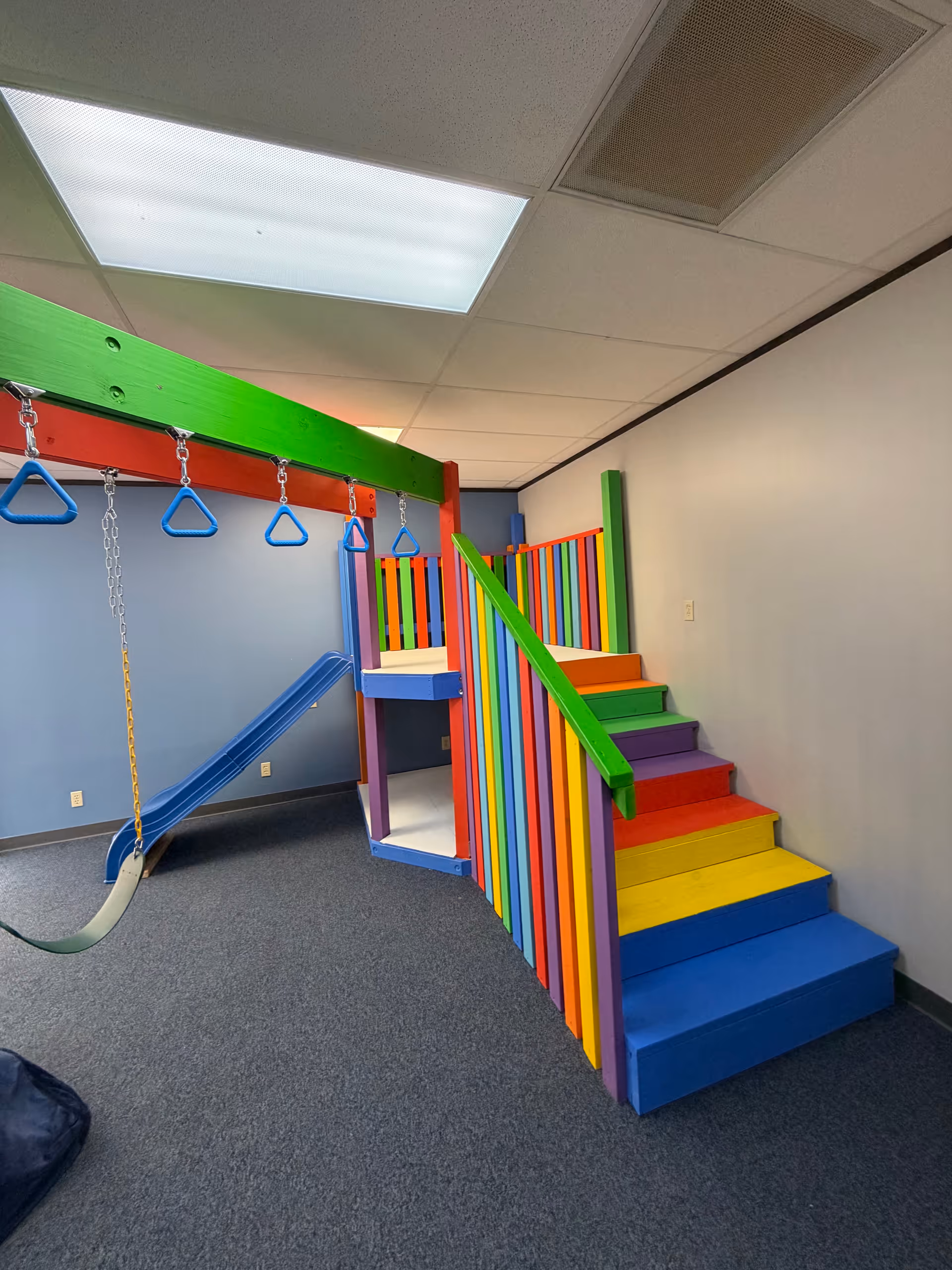 Bright rainbow indoor playground with stairs, slide, and swing in a facility.