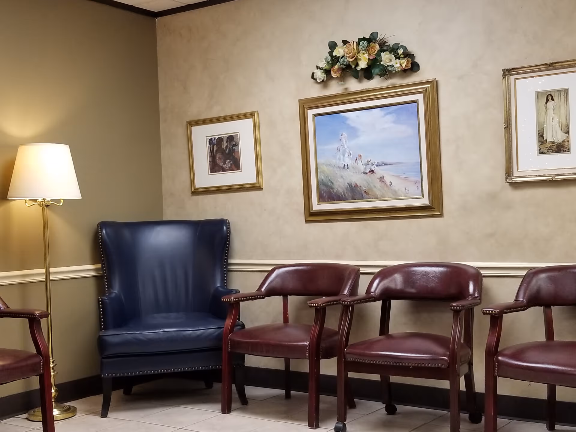 A quiet waiting area inside a senior care facility, with burgundy chairs and wall art.