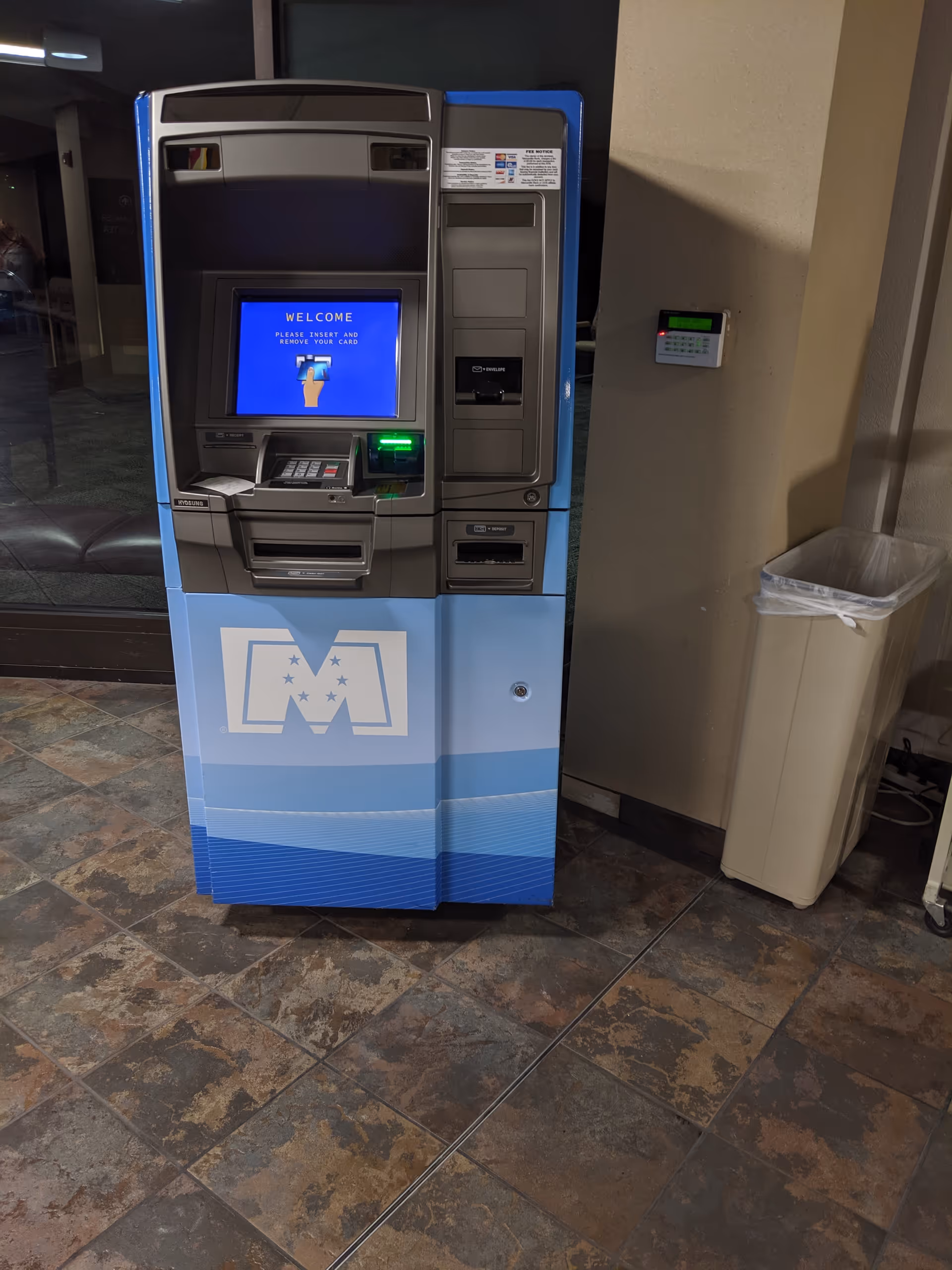 Blue ATM kiosk in Blessing Hospital lobby, near a trash can.
