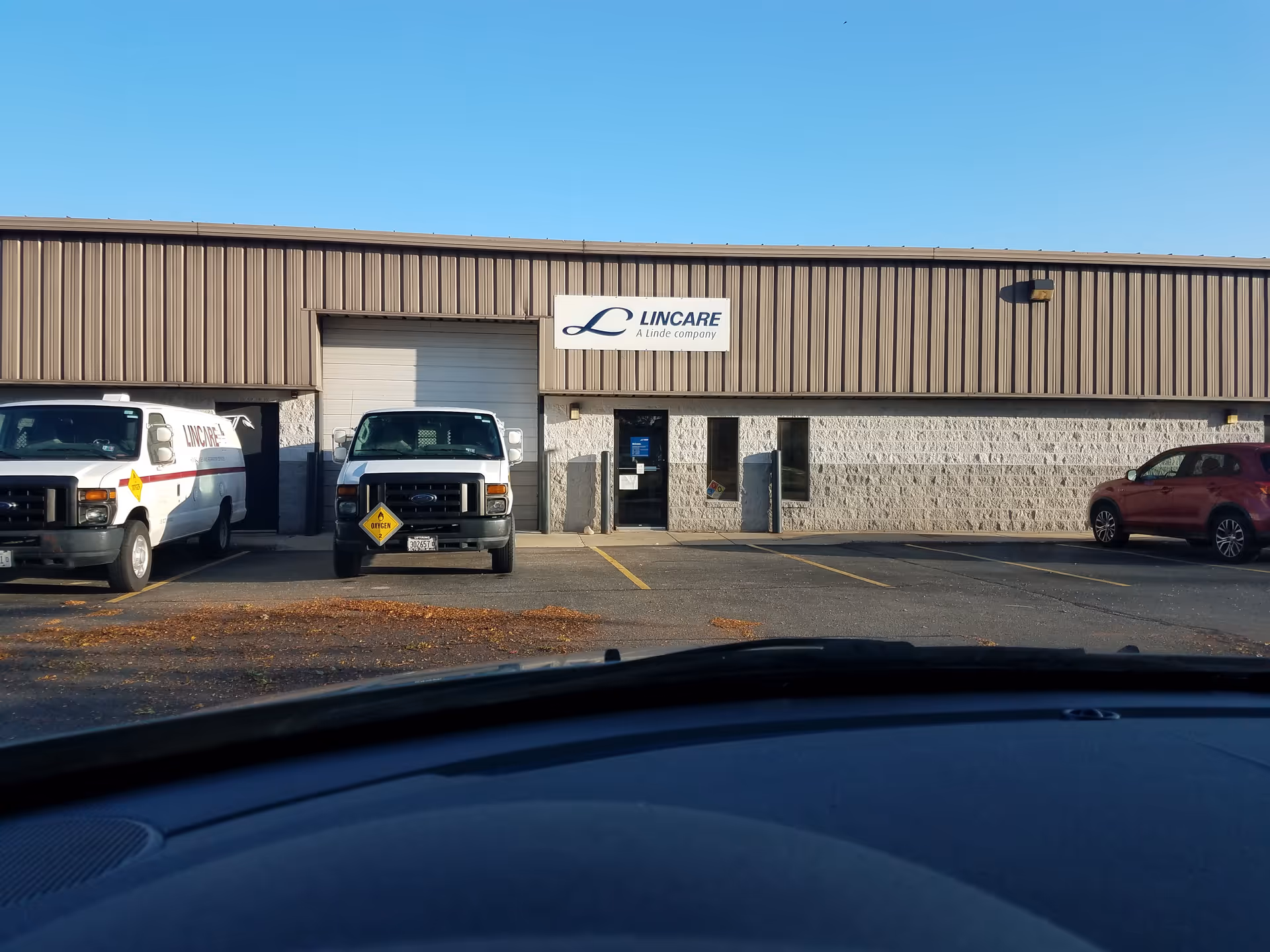 Exterior view of a LINCARE facility with two white vans parked in front.