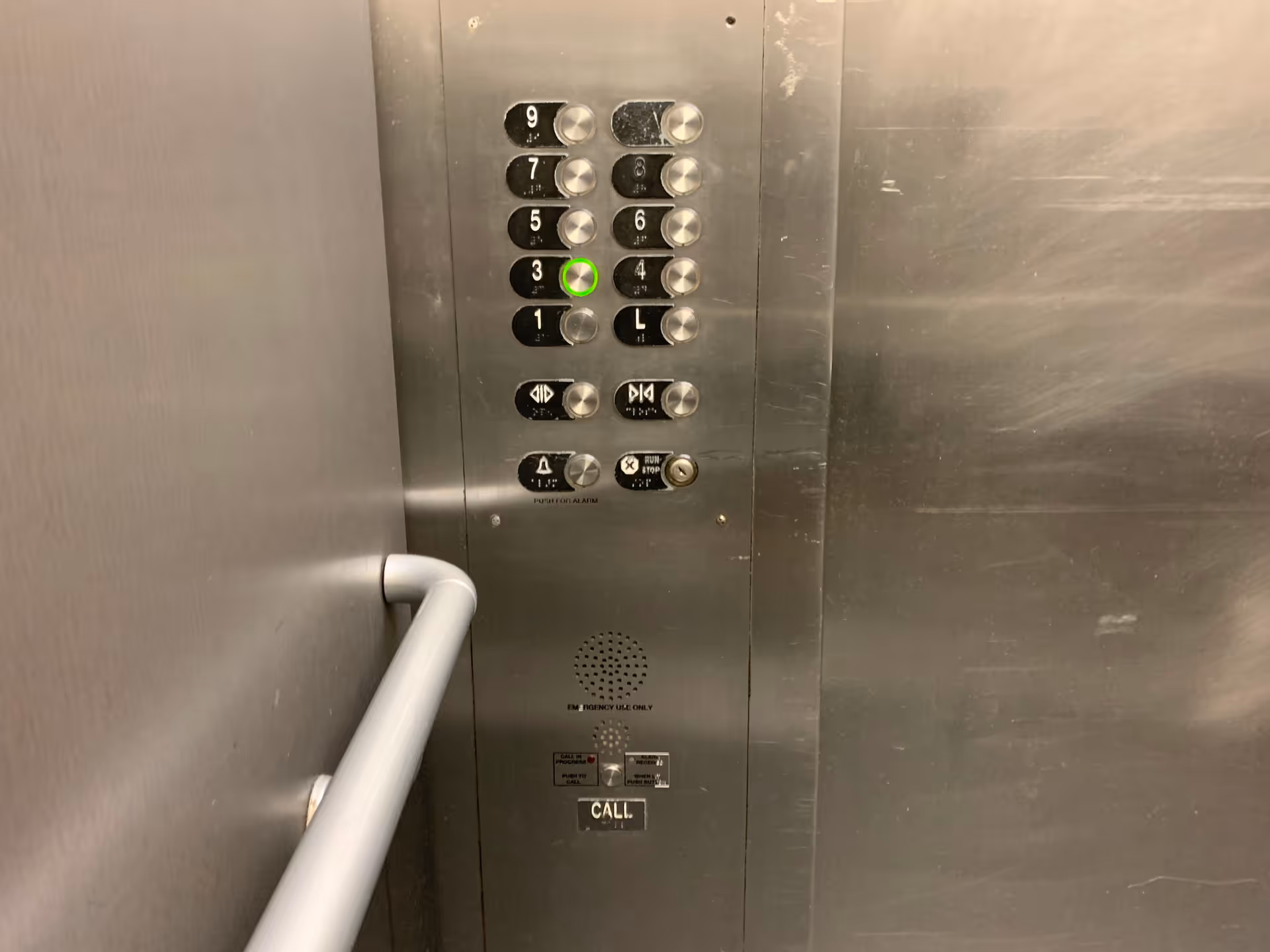 Elevator control panel with floor buttons and a railing inside.